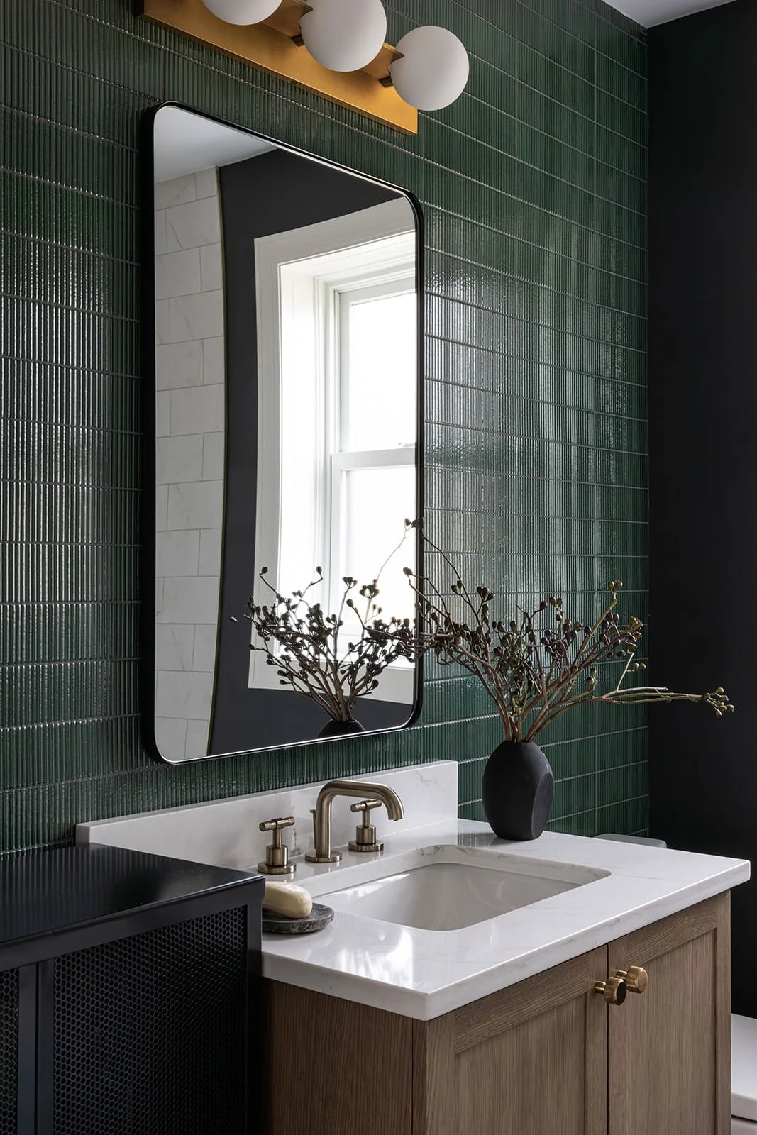 dark green tiled bathroom with brass accents, wood vanity and marble top