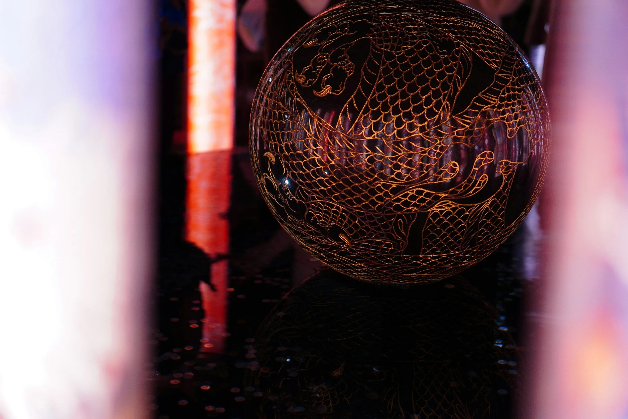 A spherical decorative object with an intricate gold dragon design on a black background, reflecting on a glossy surface.