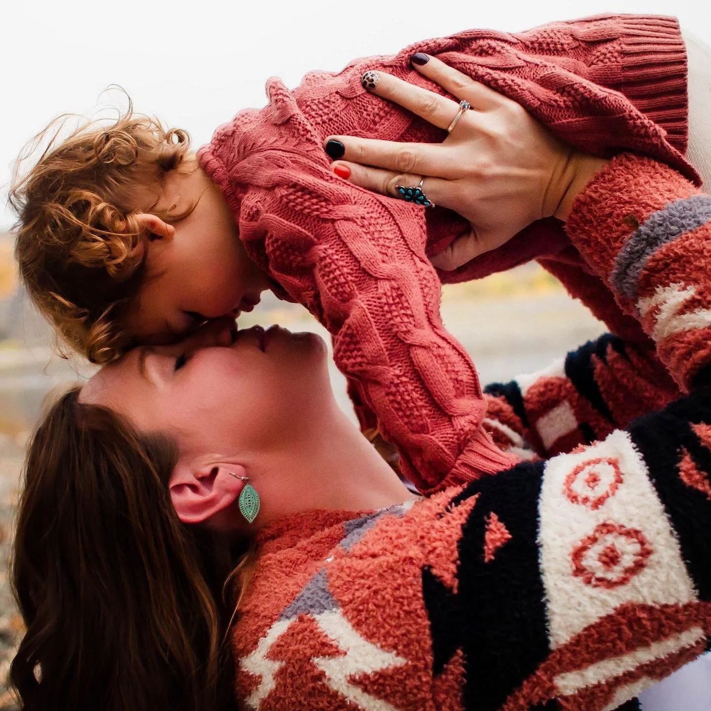 Two women with red hair in a passionate embrace and kiss while holding a young boy with curly red hair, who is about to kiss or touch their faces.