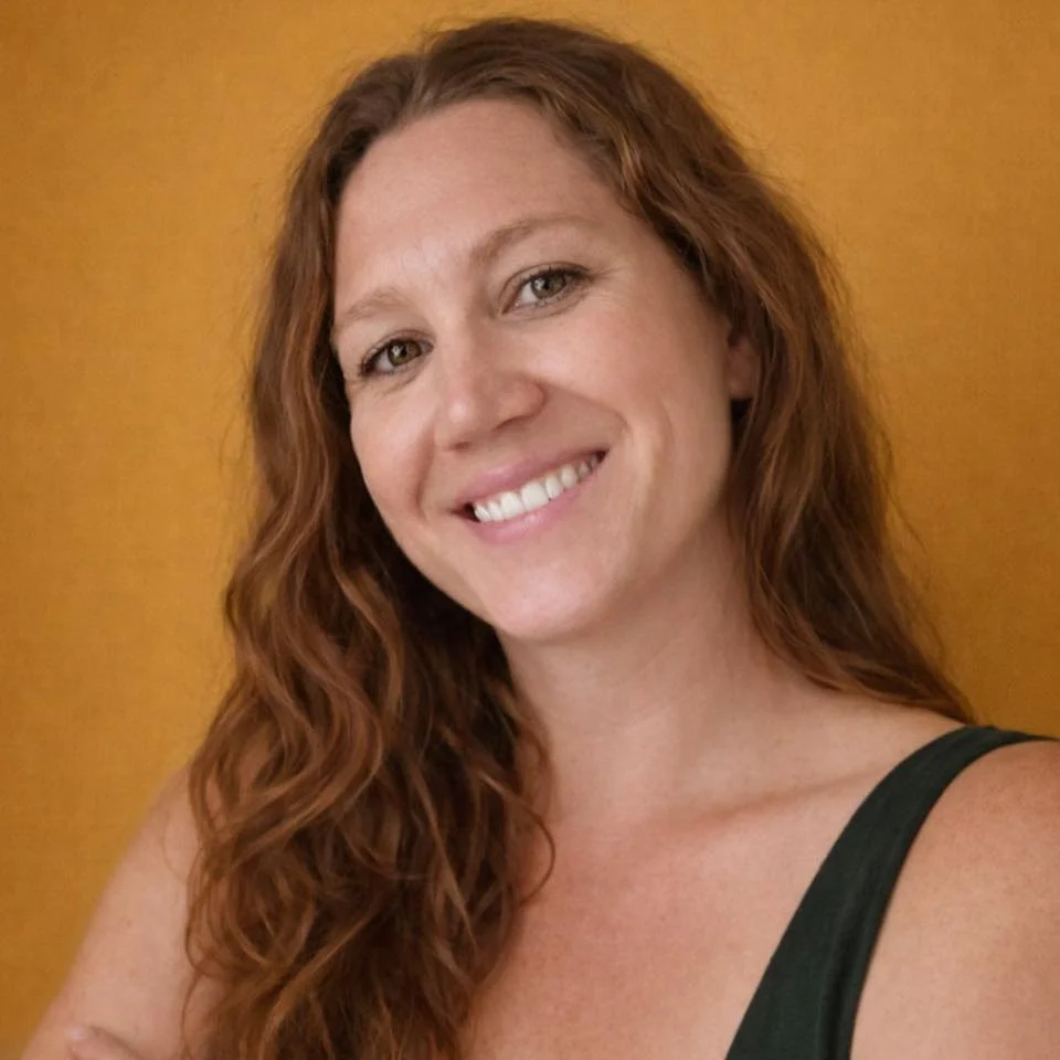 A woman with long, wavy red hair smiling against a wooden background.