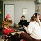 Four young women sitting together in a cozy room, socializing, some with drinks, with relaxed atmosphere.