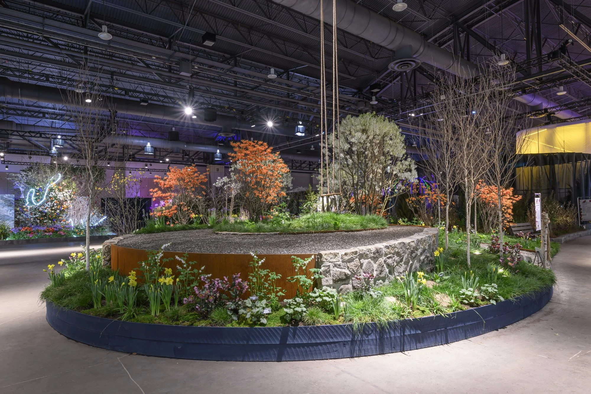 Indoor garden exhibit with colorful trees, flowers, a swing, and decorative lighting.