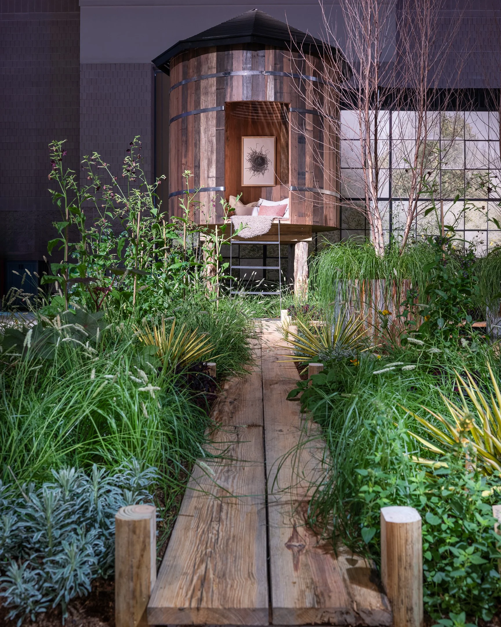 A small wooden house built on stilts surrounded by lush greenery, with a pathway leading to the entrance.