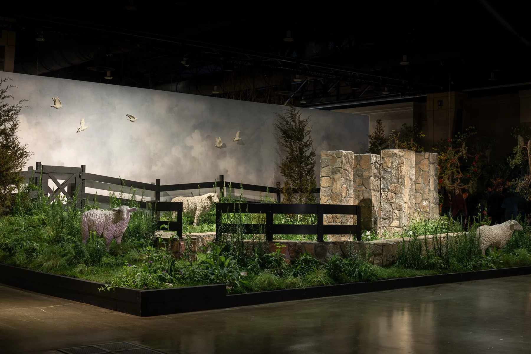Indoor exhibit with artificial sheep, trees, and a stone wall, designed to resemble a rural farm scene.