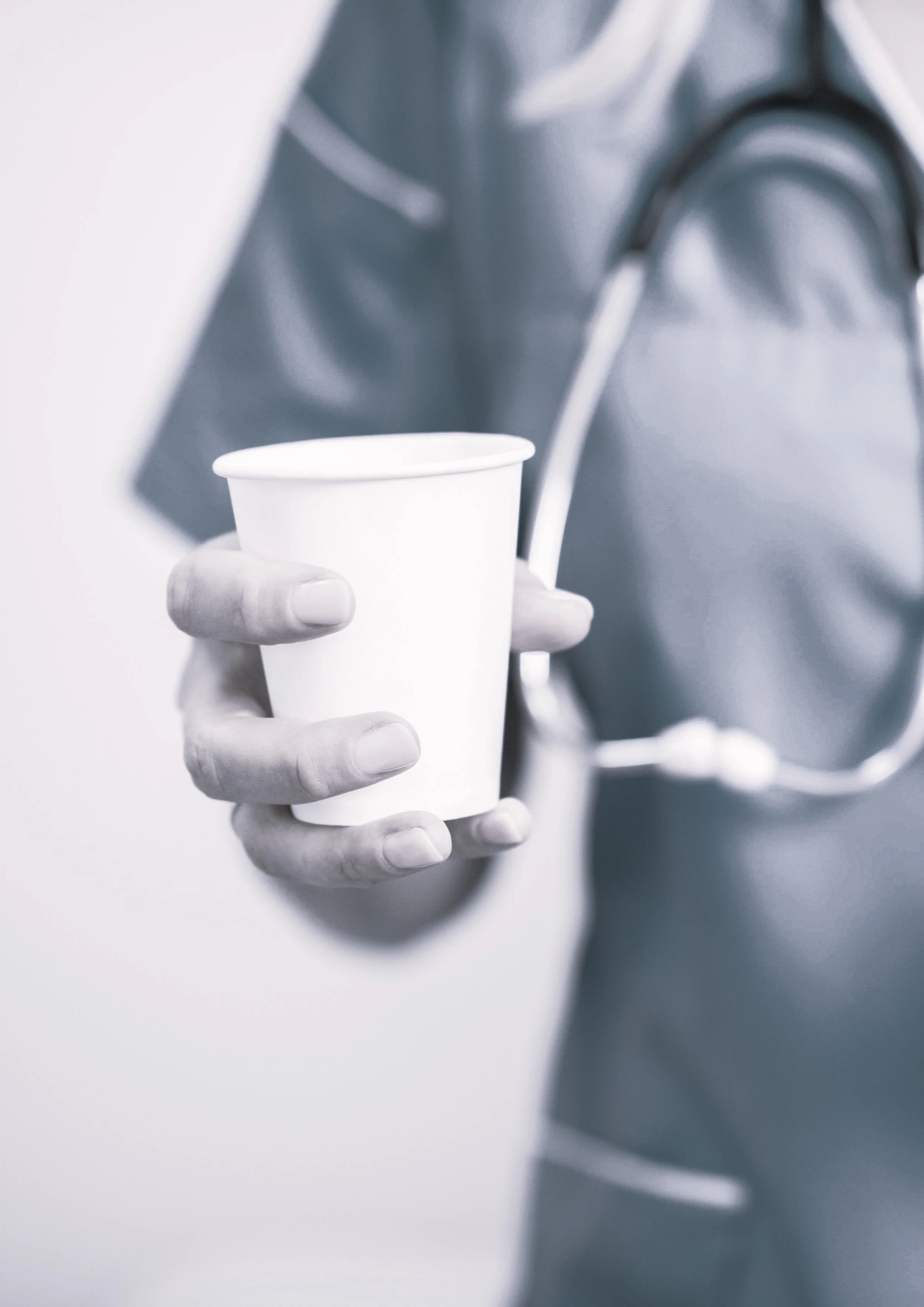 A person in medical scrubs holds a white paper cup, with a stethoscope around their neck.