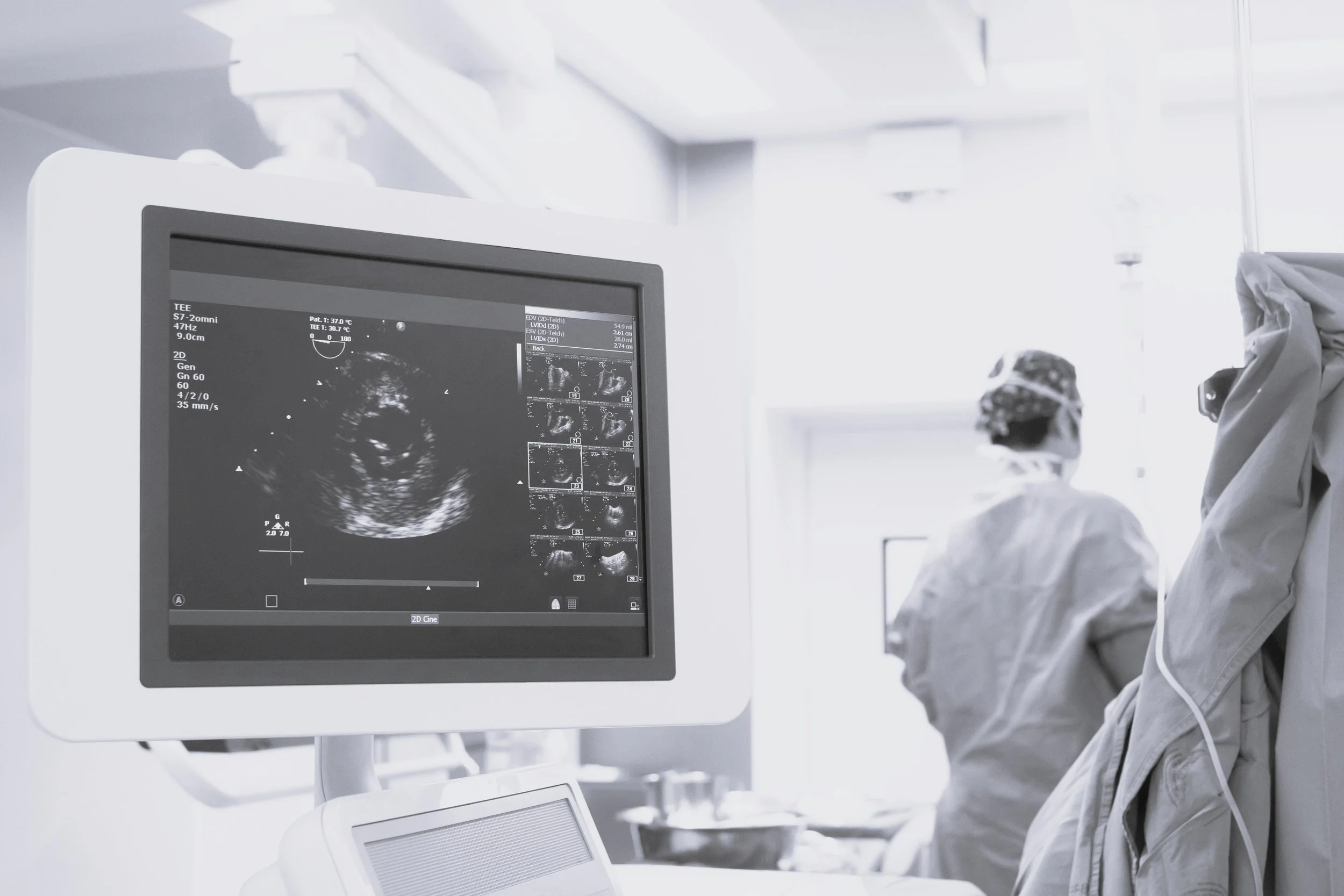 A medical professional in protective gear looking at an ultrasound monitor in a clinical setting.
