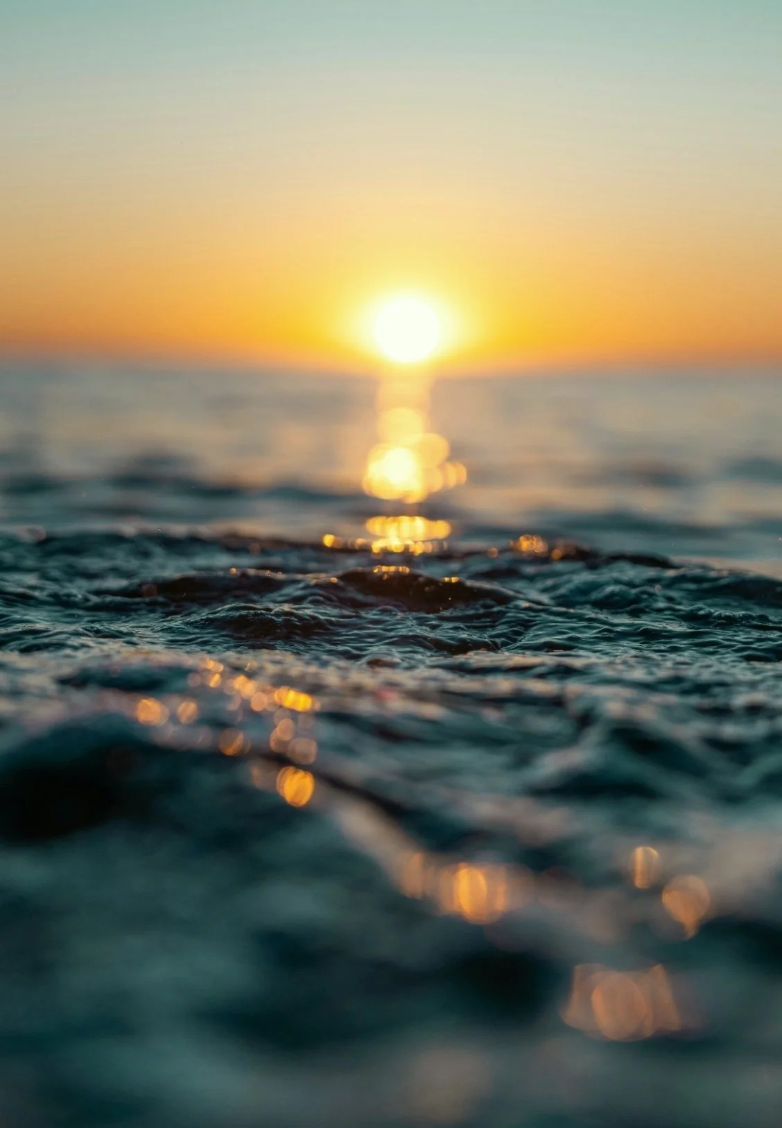 Sunset over the ocean with blurred water in the foreground and the sun low on the horizon.