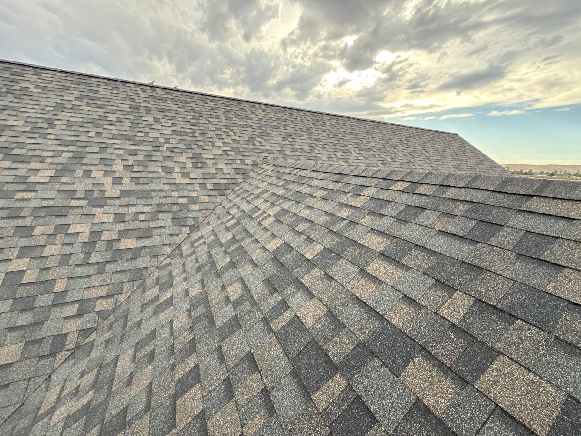 Close-up view of a house roof with asphalt shingles under a cloudy sky.