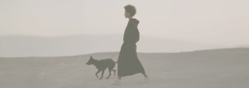 A woman walking a dog on a beach or open plain during sunset or sunrise.