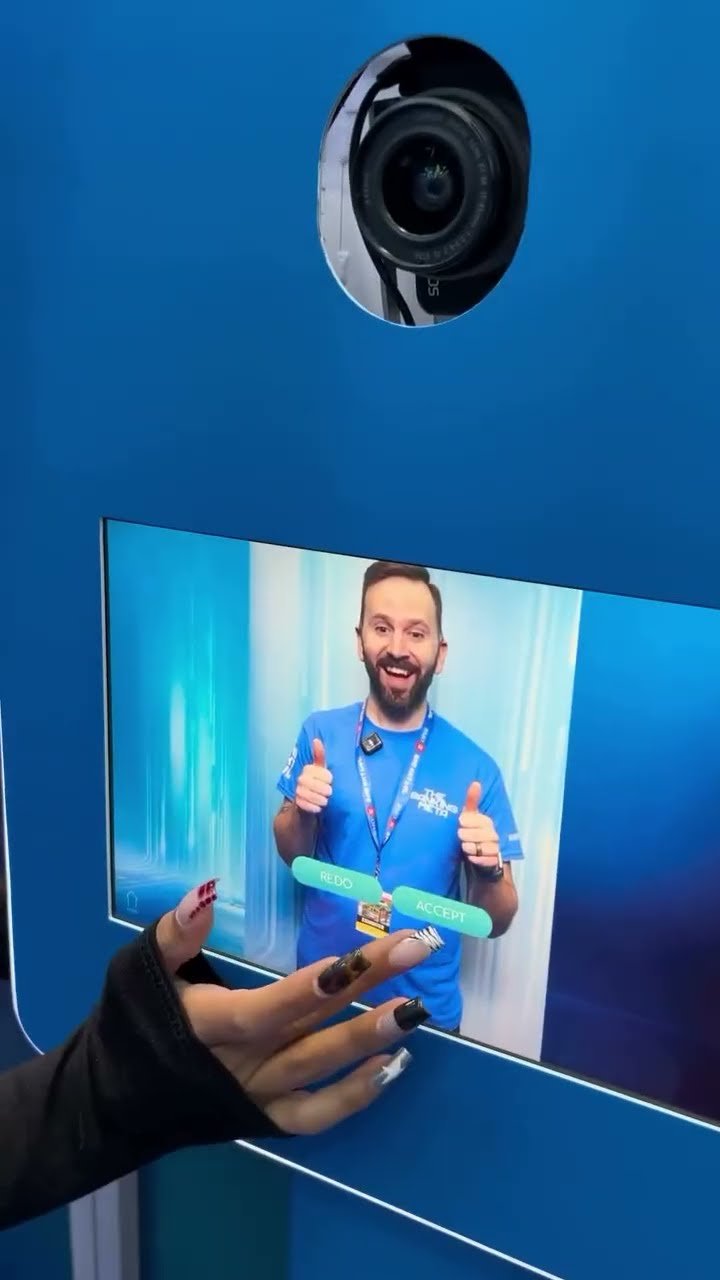 A person with painted nails presses a touchscreen with options to 'REJECT' or 'ACCEPT' on an interactive display, showing a smiling man giving thumbs up.