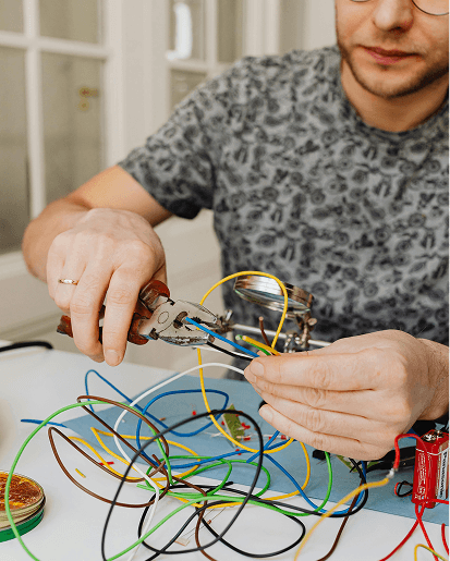 Person working on an electronics project with colorful wires and tools on a white table.