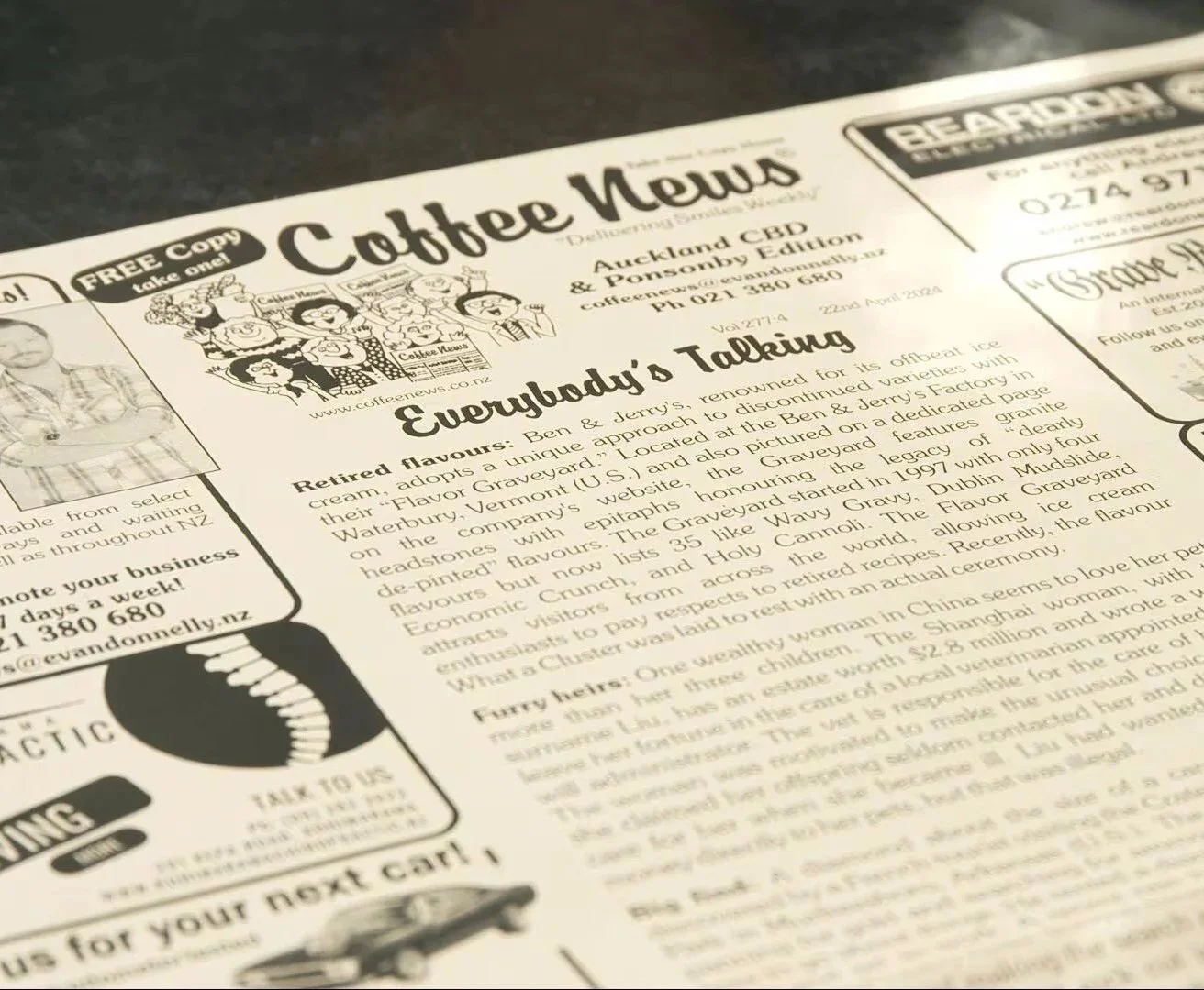 A newspaper titled Coffee News with an article about Ben & Jerry's themed ice cream flavors and their history, including a cartoon illustration of a group of people holding coffee cups at the top.