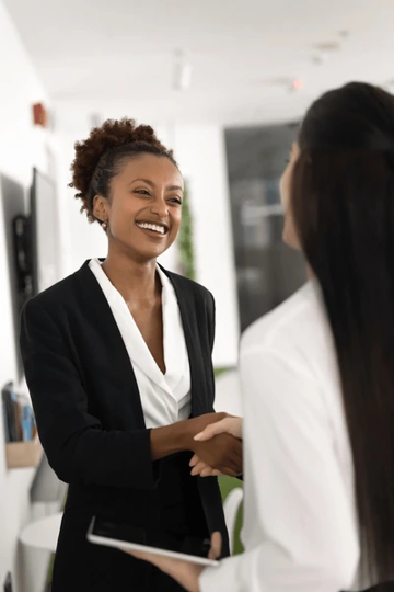 Two women shaking hands and smiling in a professional setting.