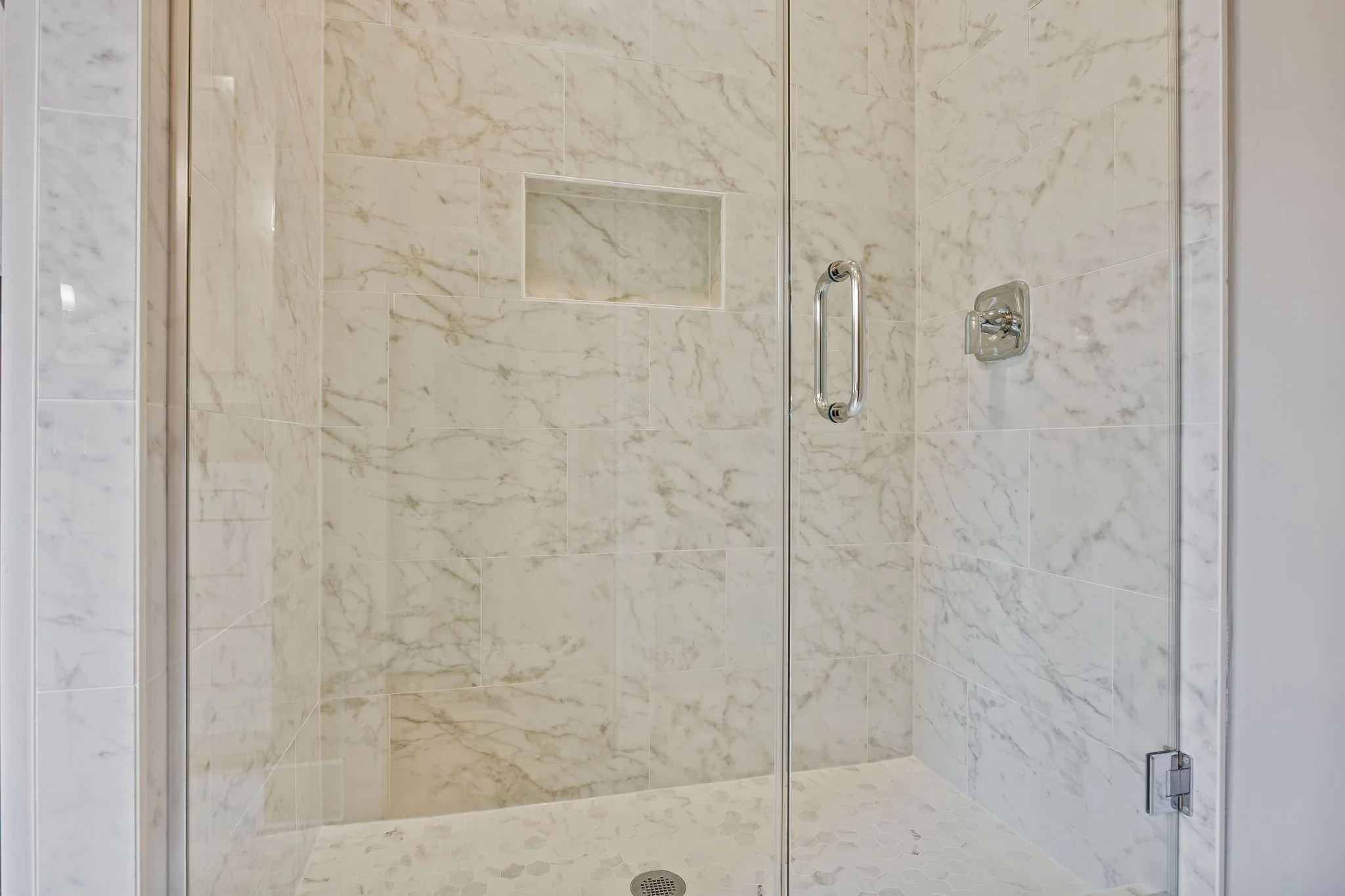 Shower with marble tiles, a built-in niche, a glass door, and chrome fixtures.