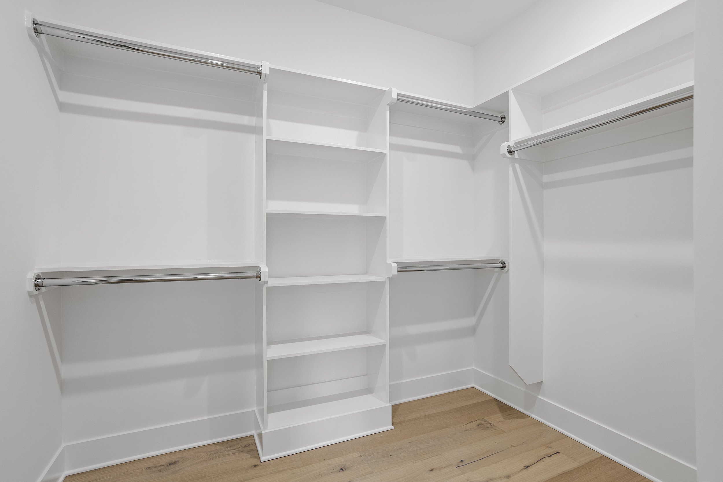 Empty white walk-in closet with shelves and hanging rods, and a wood floor.