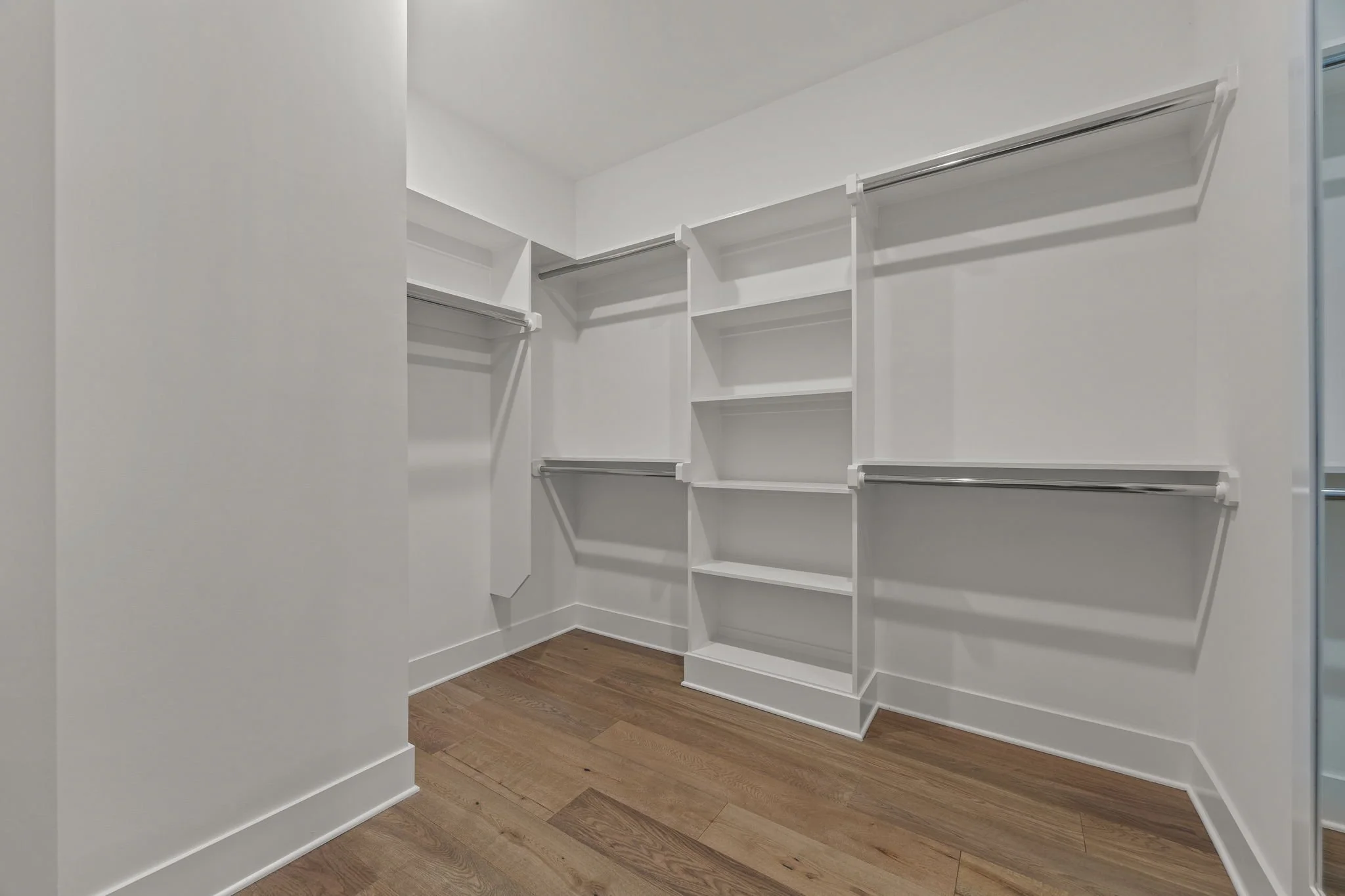 Empty white walk-in closet with multiple shelves and hanging rods, wooden floor.