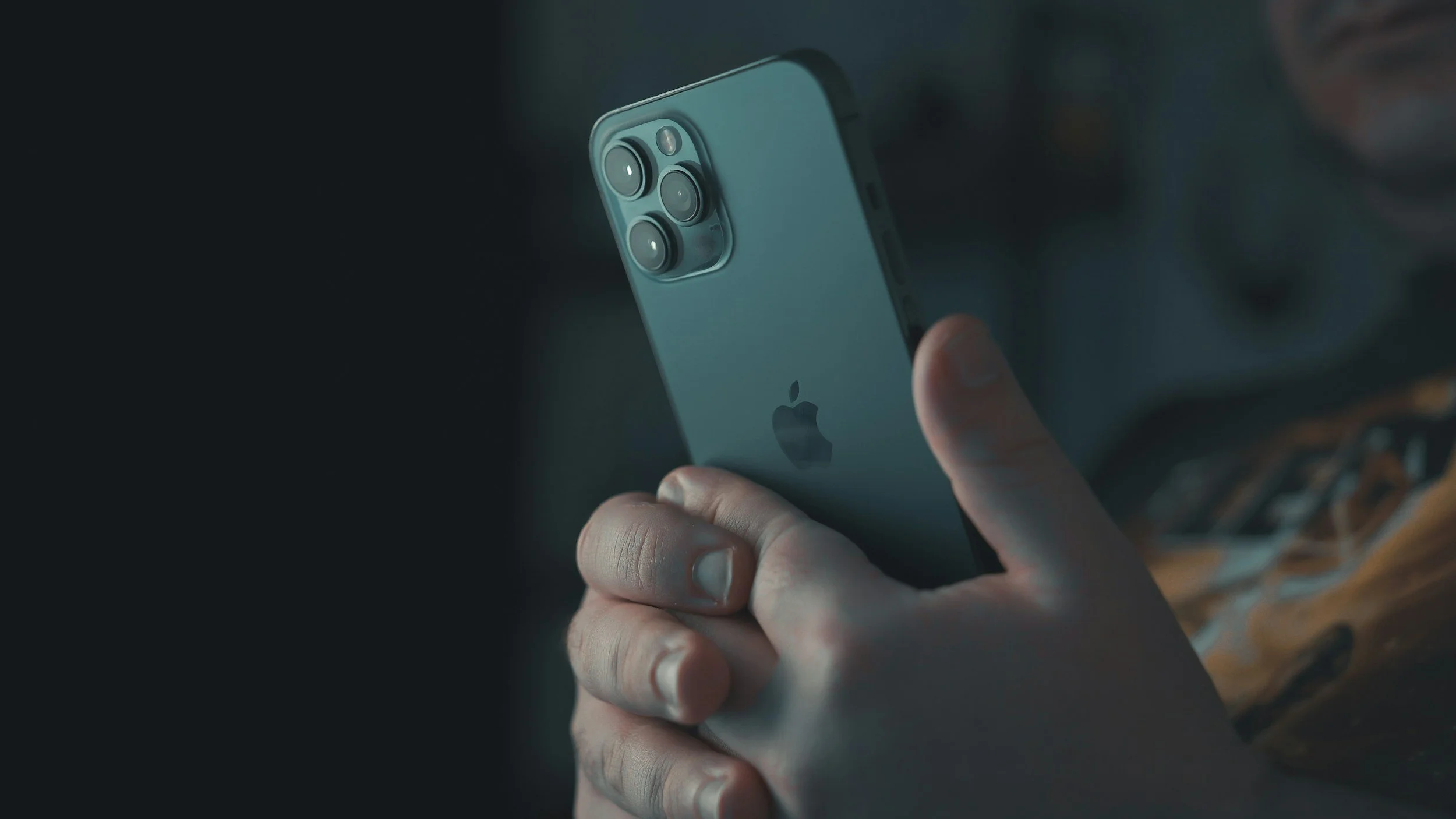 Close-up of a person holding an iPhone with a triple-camera system, with fingers gripping the phone and the Apple logo visible on the back.