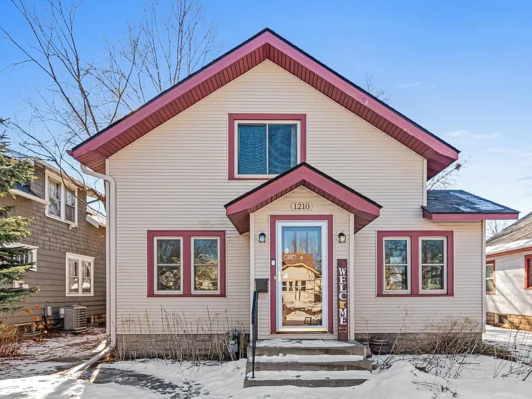 Front view of a two-story house with cream siding and pink trim, snow on the ground, and trees in the background.