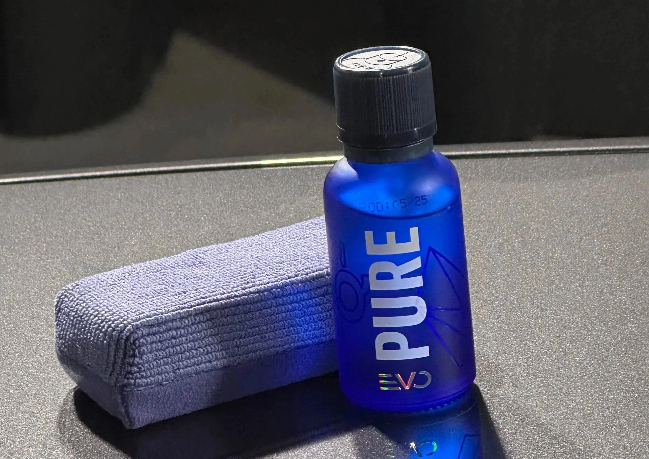 A blue bottle labeled 'PURE' resting on a textured gray towel, with a computer mouse and a metal surface in the background.