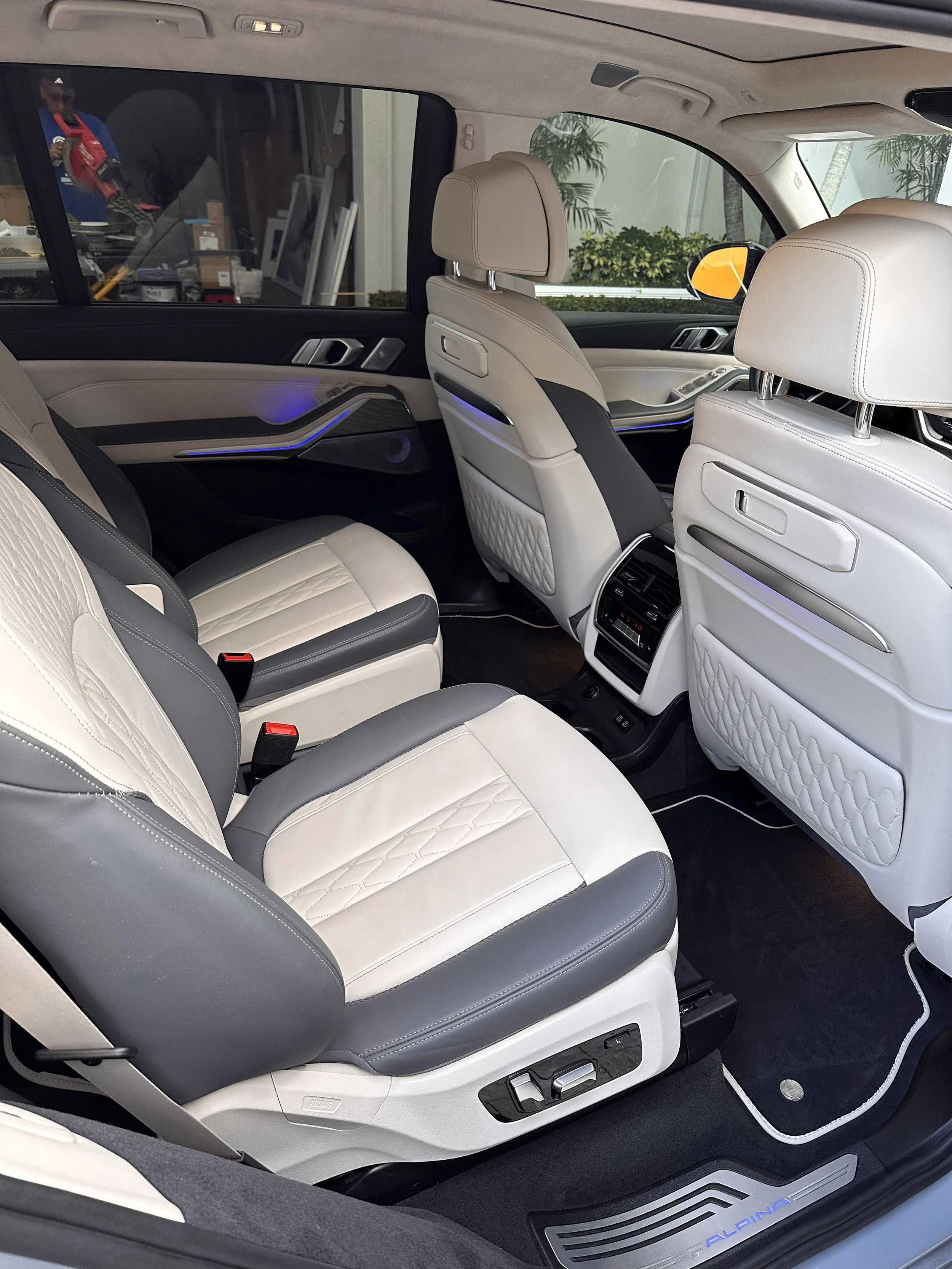 The interior of a luxury vehicle showing two front seats and part of the rear seat, all in white and black leather with quilted stitching, and illuminated ambient lighting.