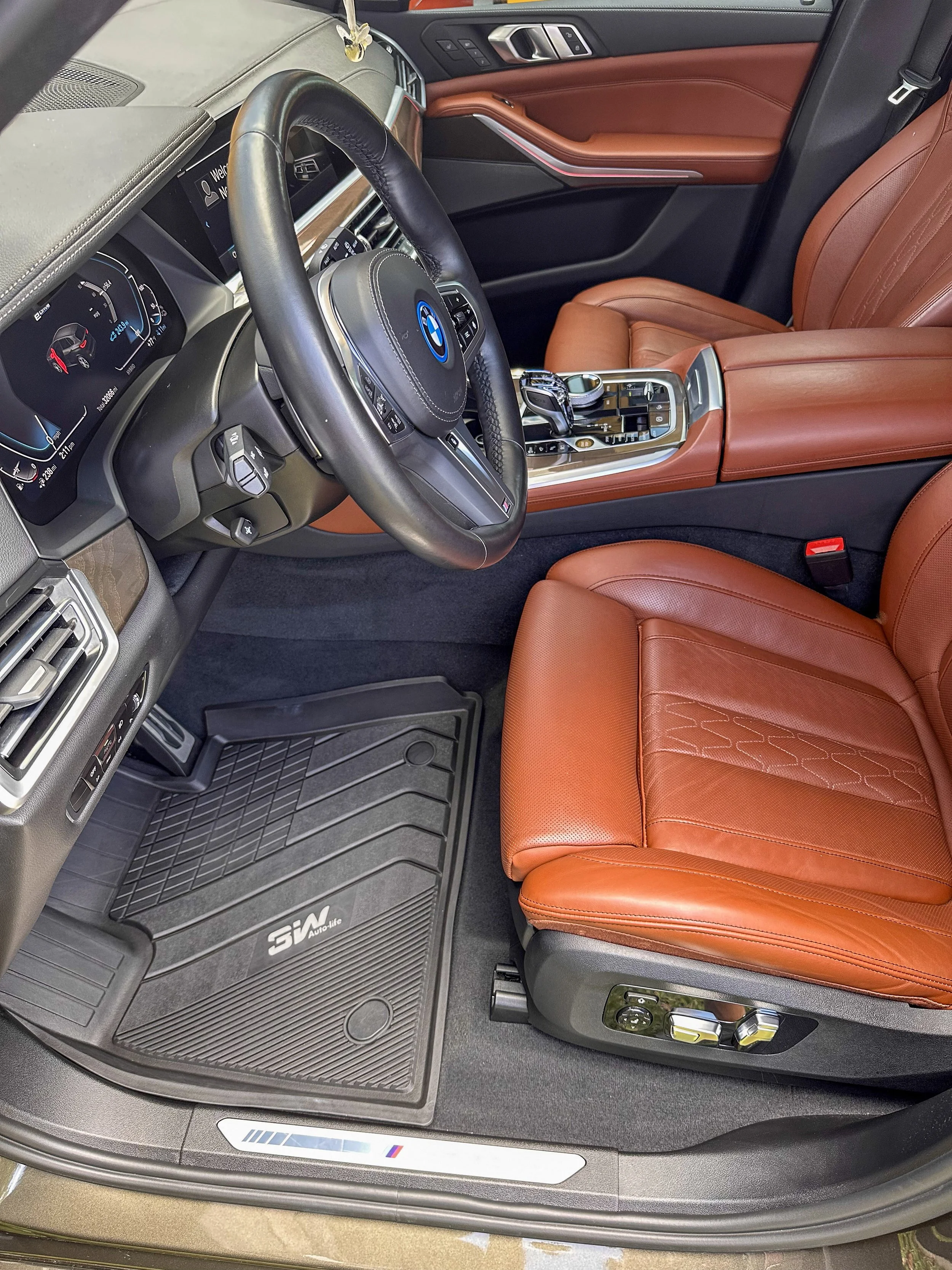 Interior of a luxury BMW car with black and brown leather seats, digital dashboard, center console with gear shifter, and floor mat with BMW M logo.