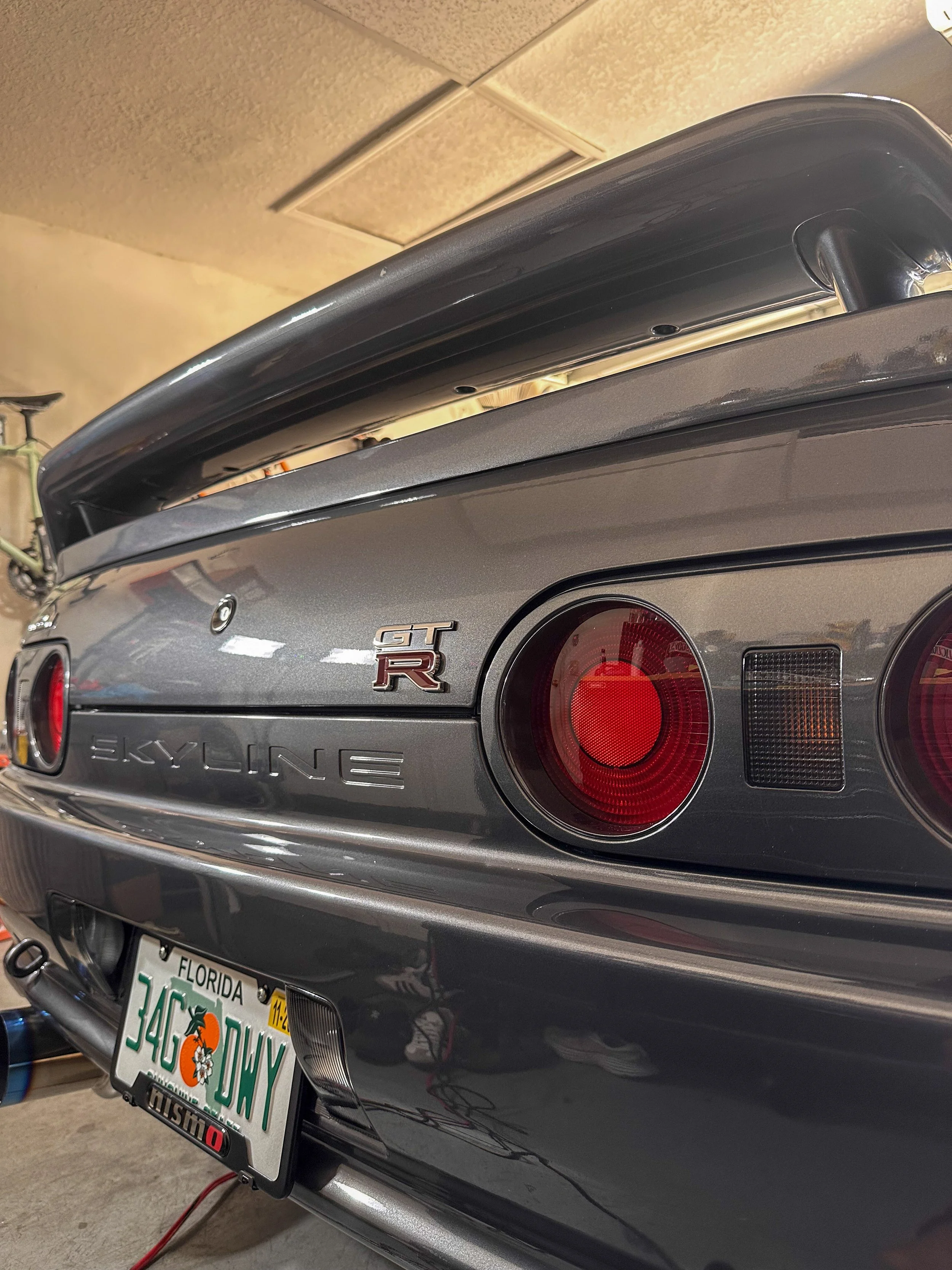 Rear view of a silver Nissan GT-R sports car with red tail lights, a spoiler, and a Florida license plate reading '3460 DXK,' parked in a garage.