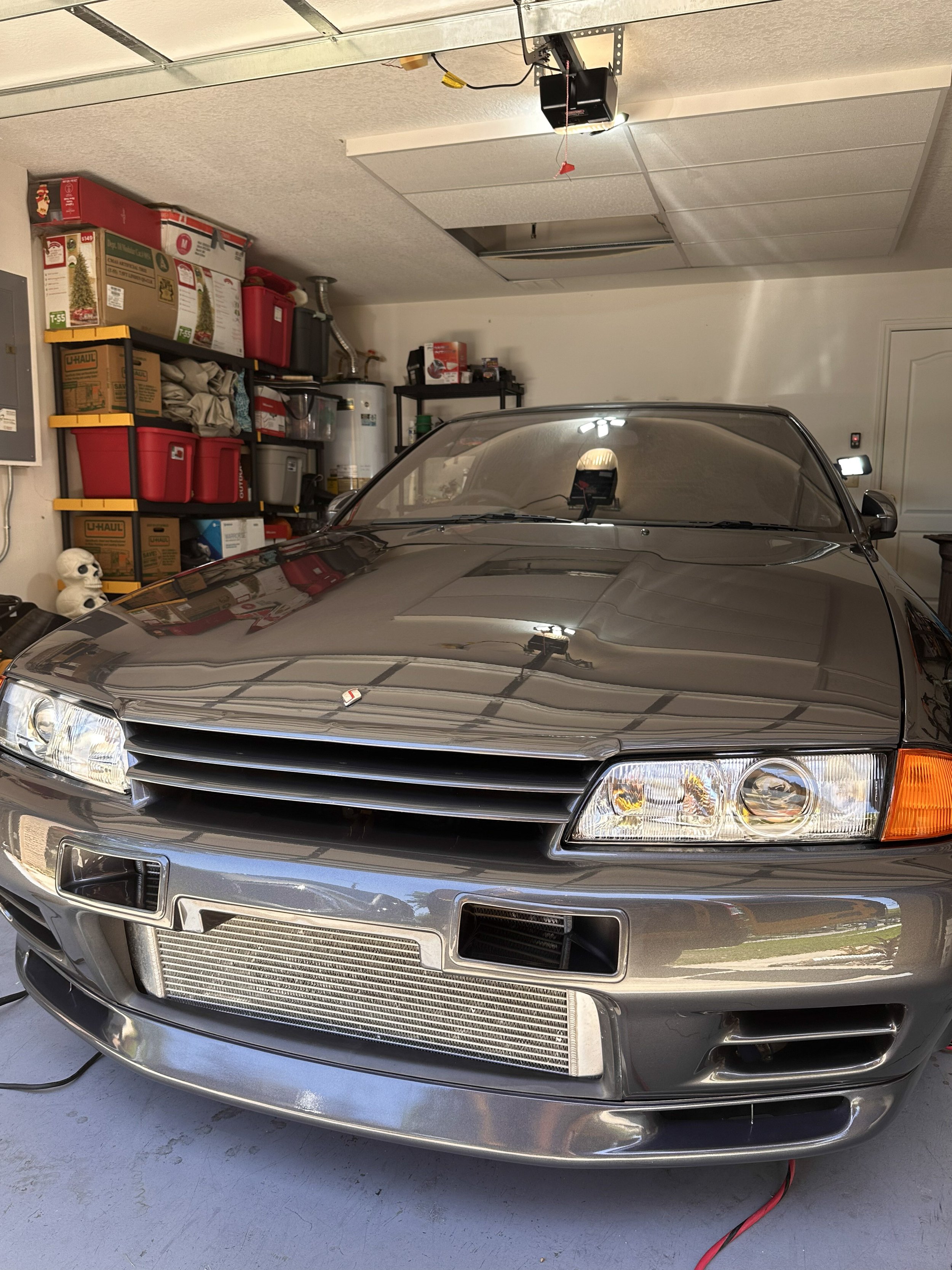 A gray car parked in a garage with boxes, storage bins, and a water heater in the background.