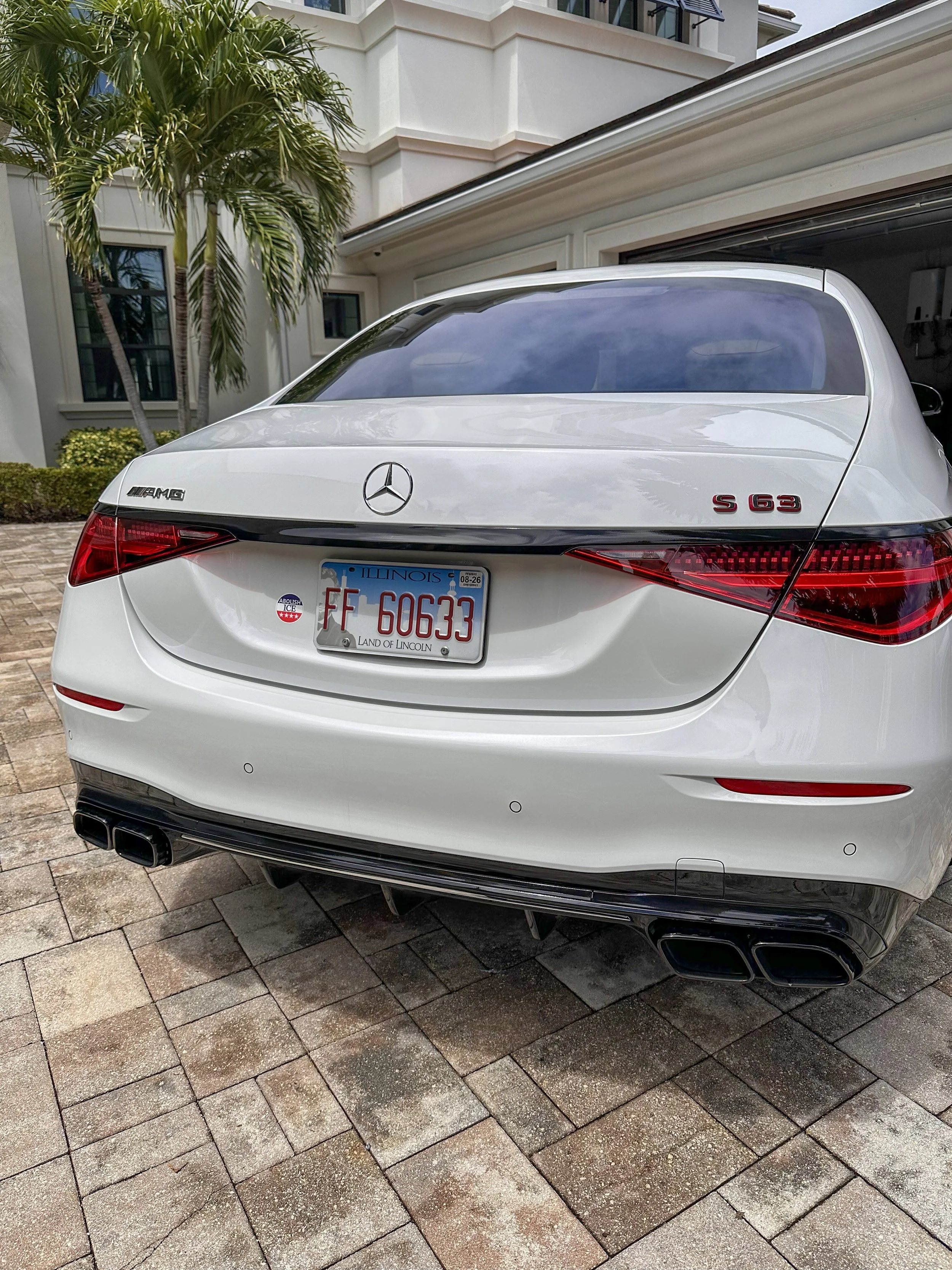 White Mercedes-Benz S-Class S 63 AMG parked outside a modern house with palm trees and a paved driveway.