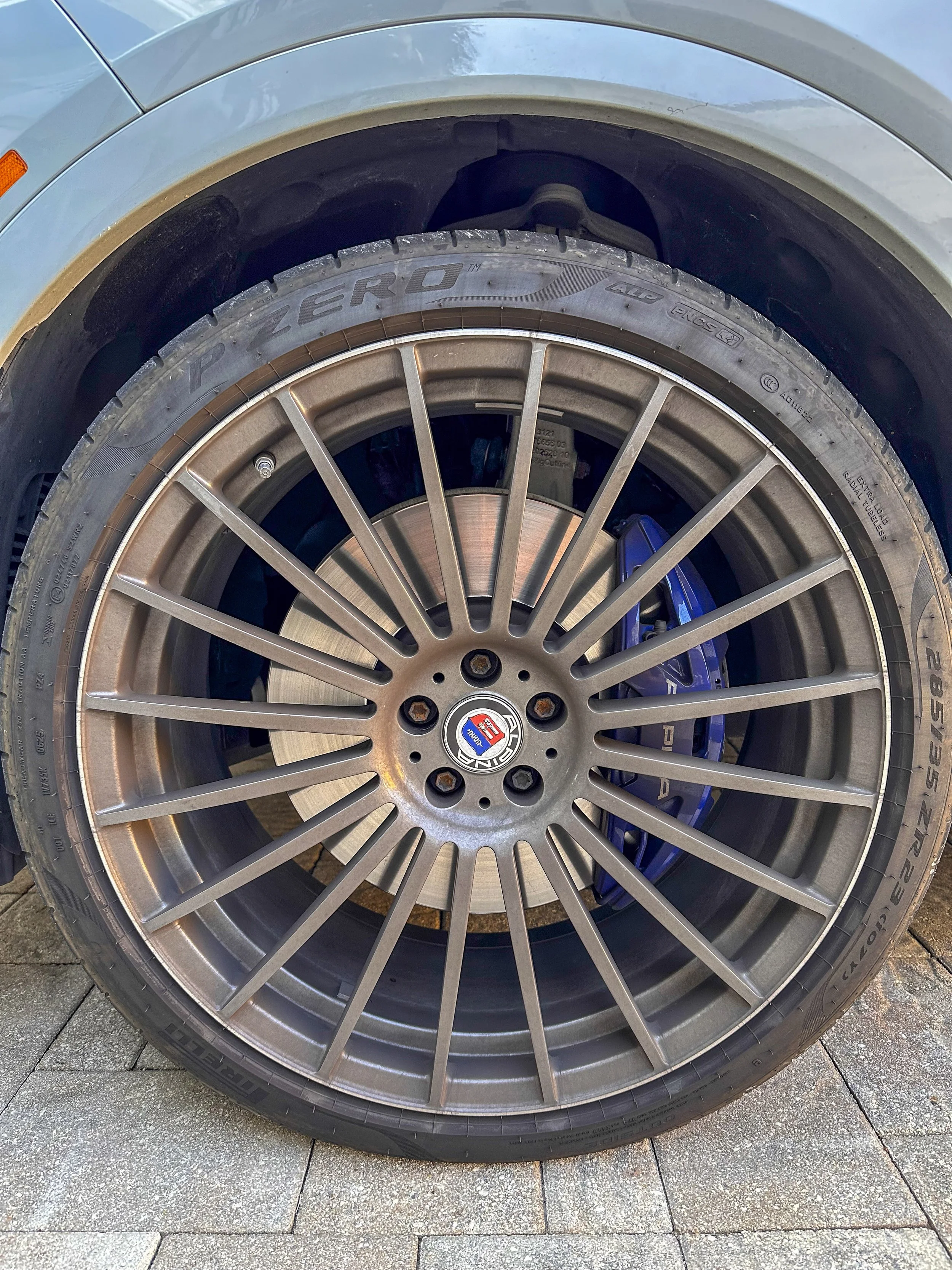Close-up of a car tire and alloy wheel, with a visible brand logo in the center, parked on a paved surface.