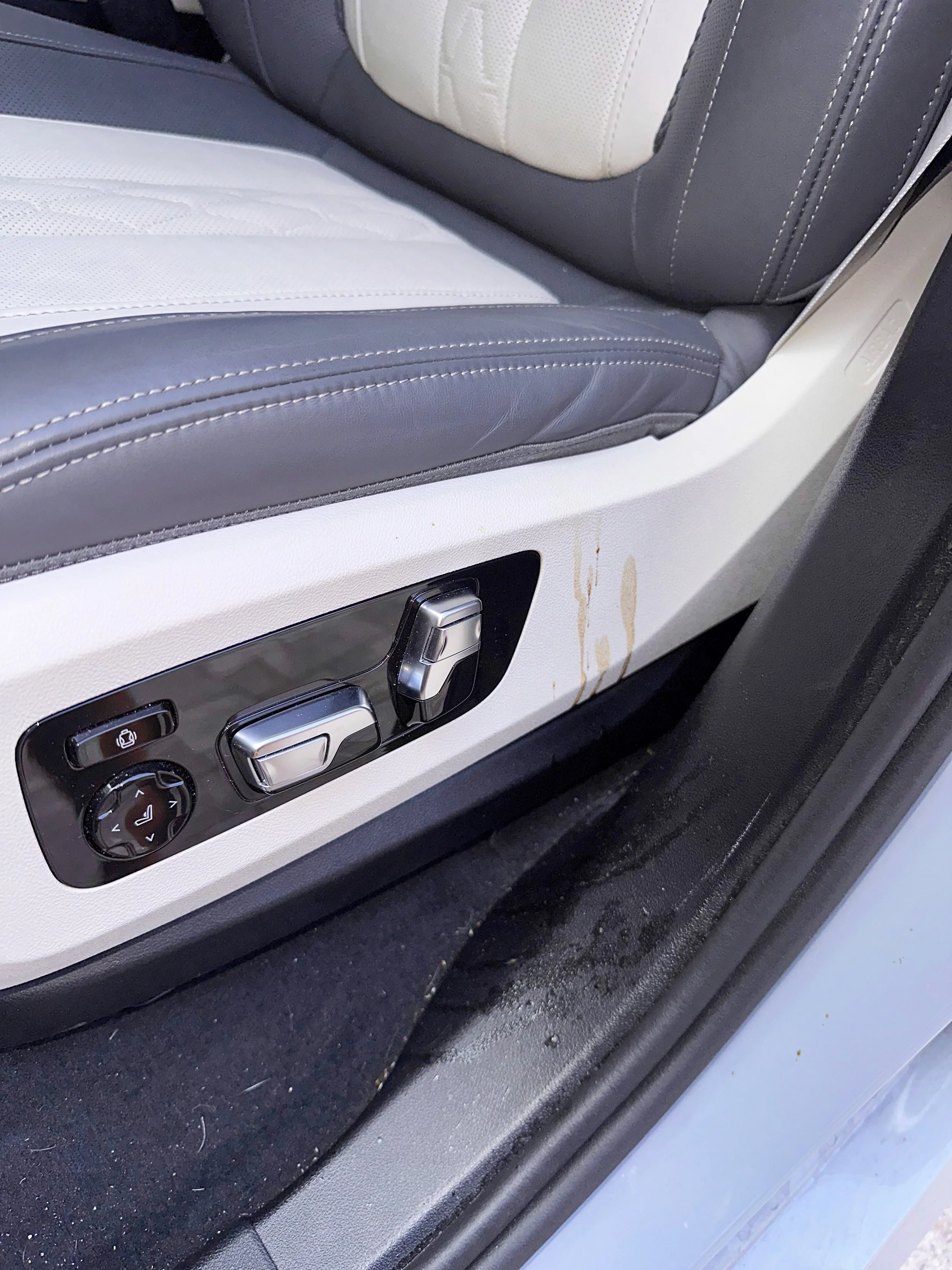 Close-up of a car seat with black and light-colored upholstery, showing control buttons on the side for adjusting the seat position.