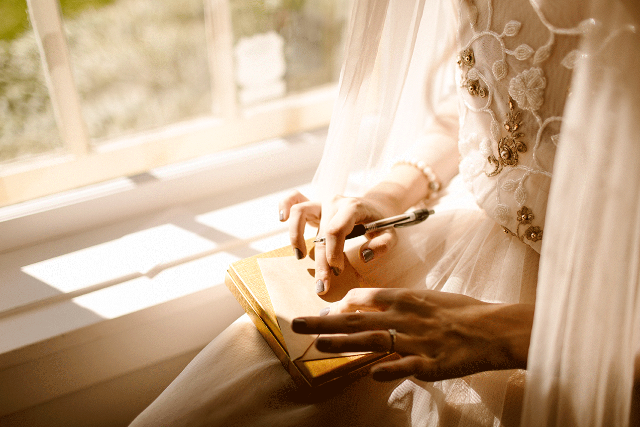 Woman writing in a notebook beside a sunlit window.