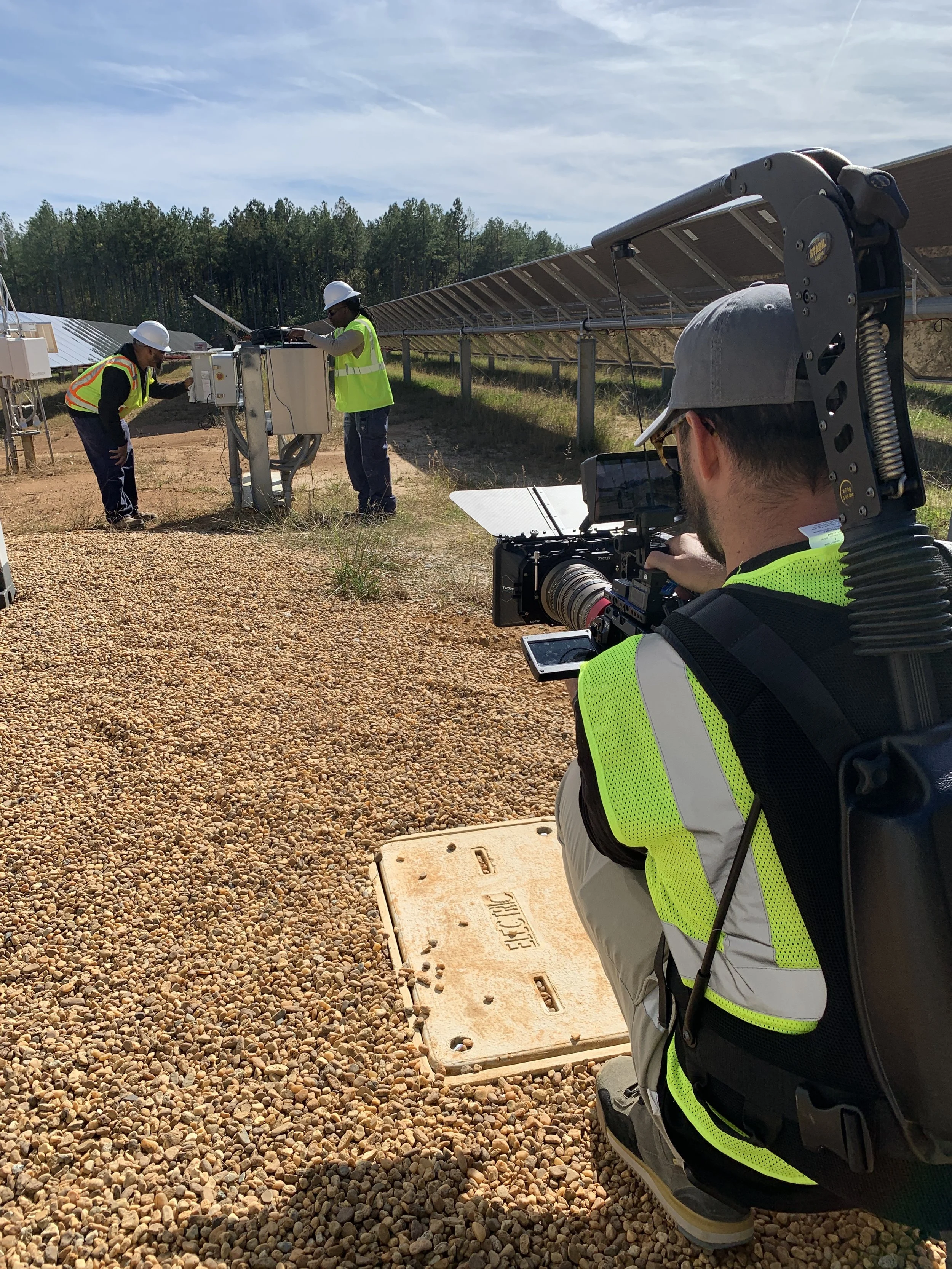 Two workers wearing safety vests and helmets inspecting equipment near solar panels in a field.