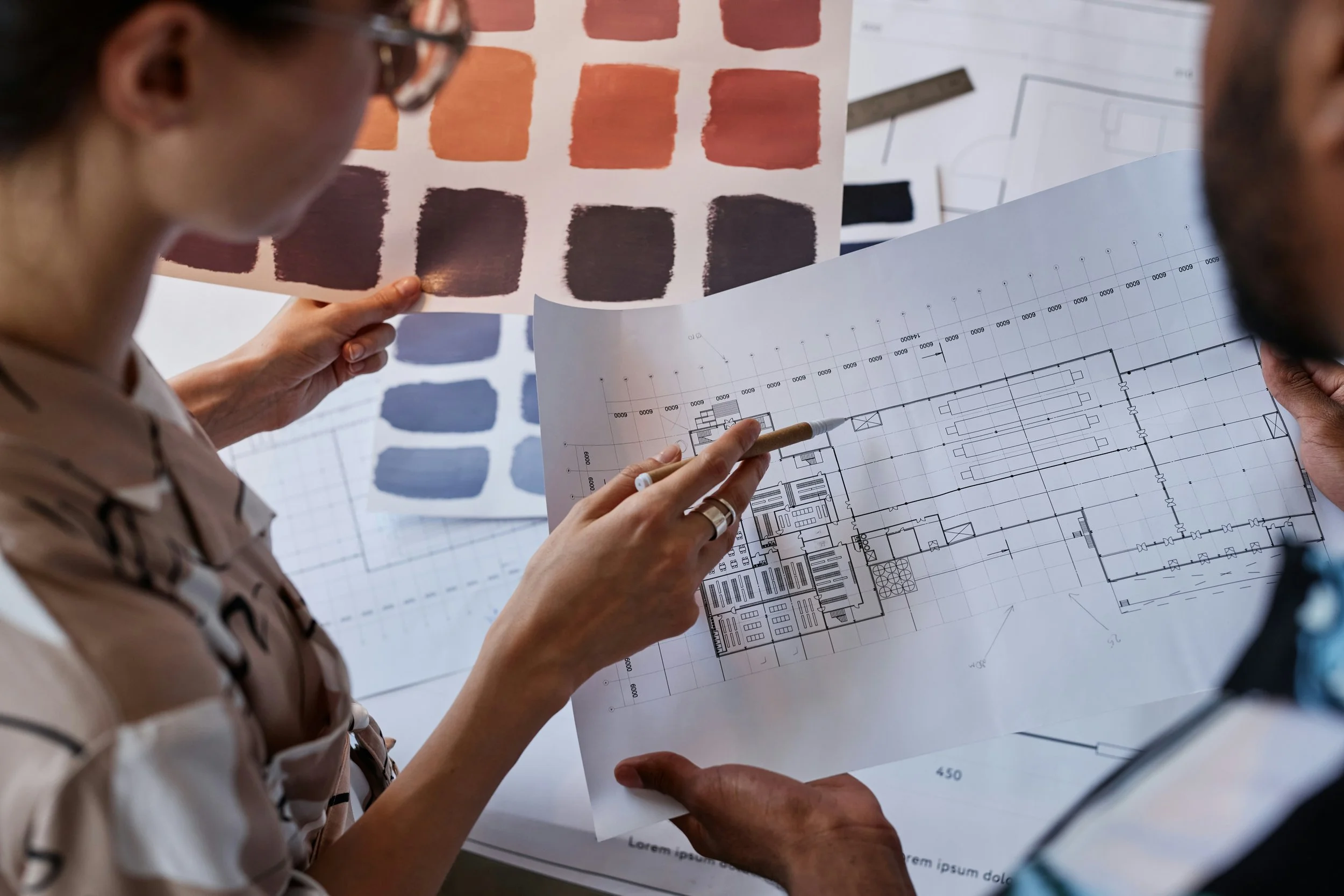 Two individuals examining architectural blueprints and color swatches in a professional setting.