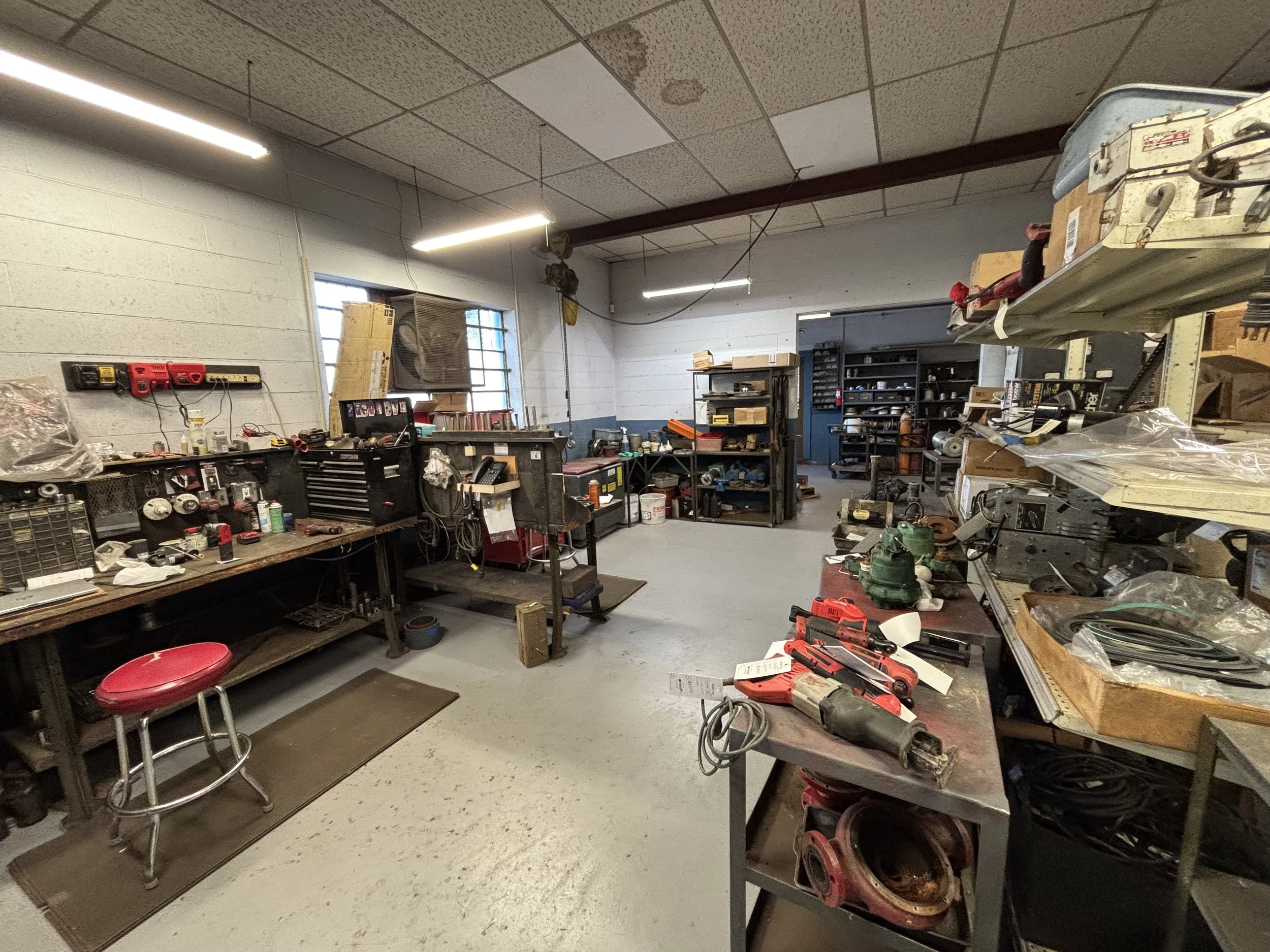 A cluttered workshop with workbenches, tools, and shelves filled with various equipment and supplies.