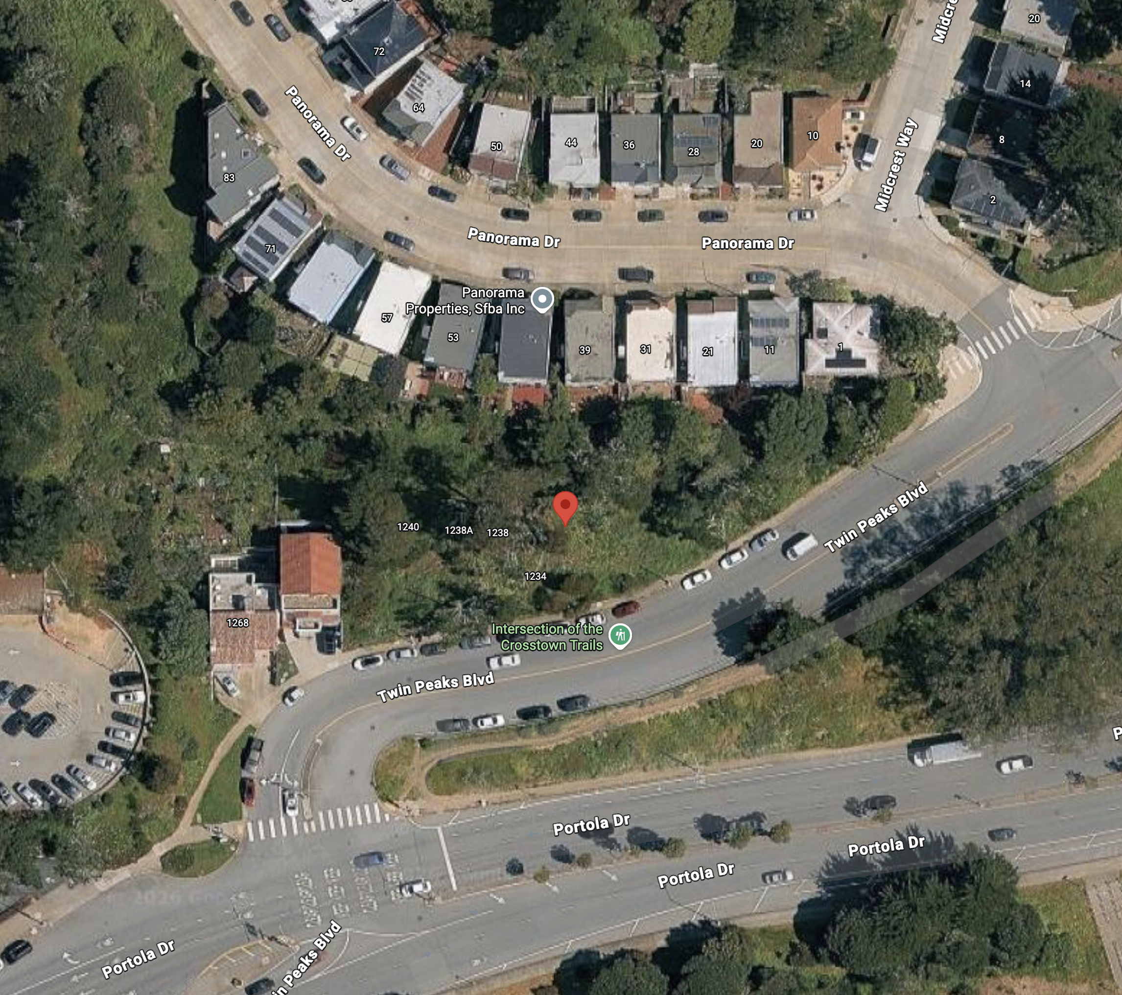 An aerial view of a residential area showing multiple houses, parked cars, streets, and trees.