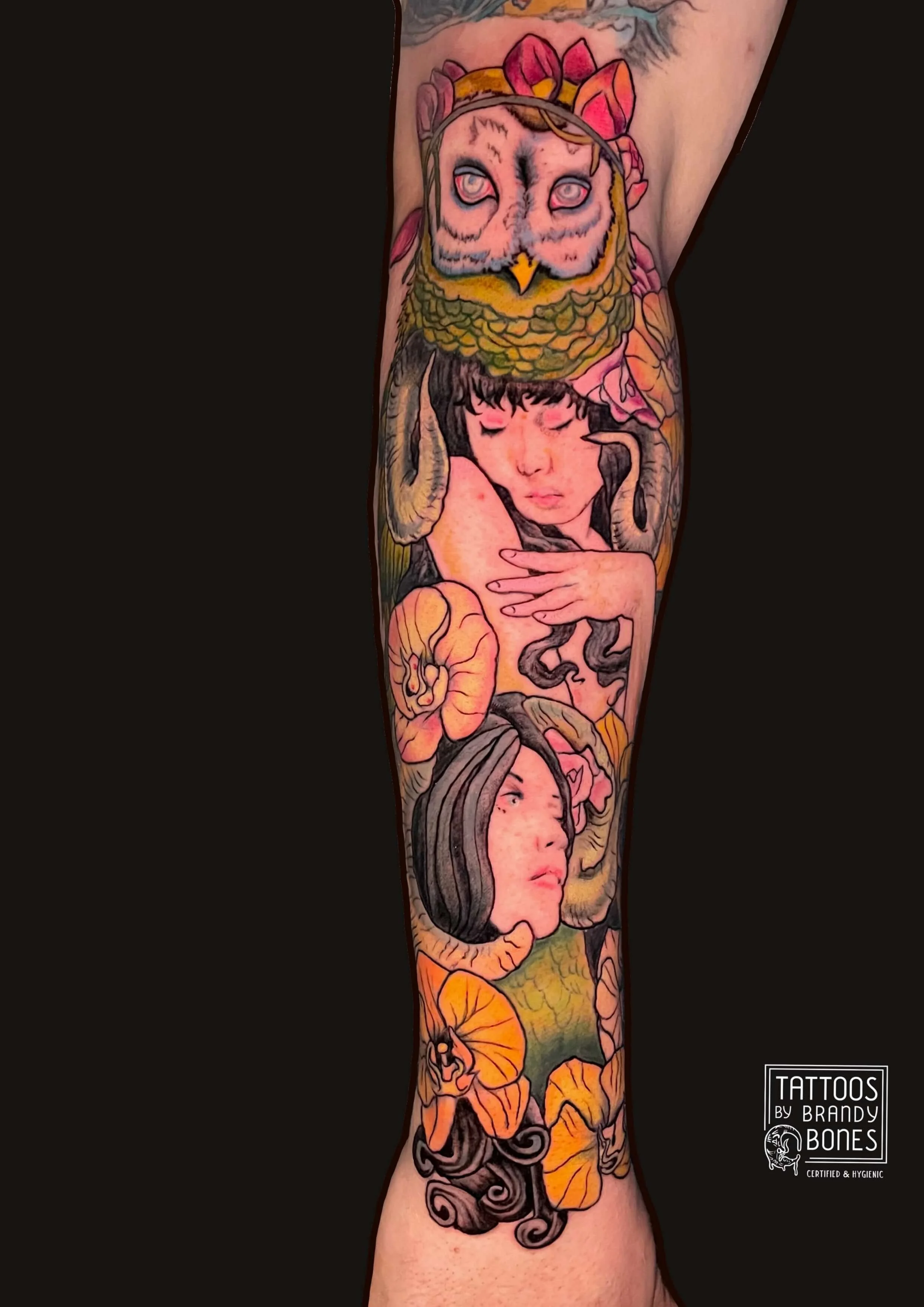 Colorful tattoo sleeve featuring a young woman's face, an owl with wide eyes, flowers, mushrooms, and swirling patterns.