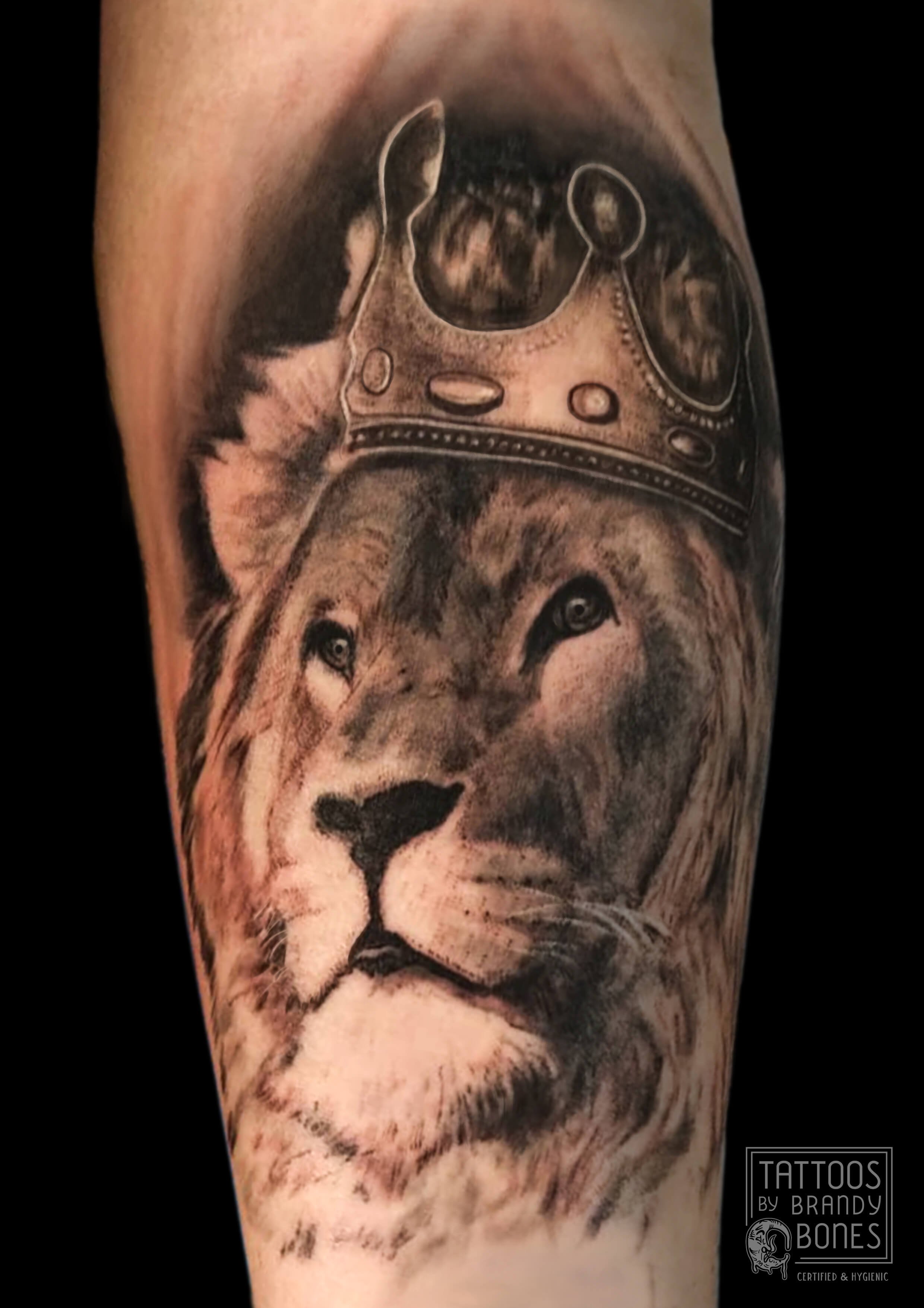 Tattoo of a realistic wolf's face with a crown above its head on a person's arm.