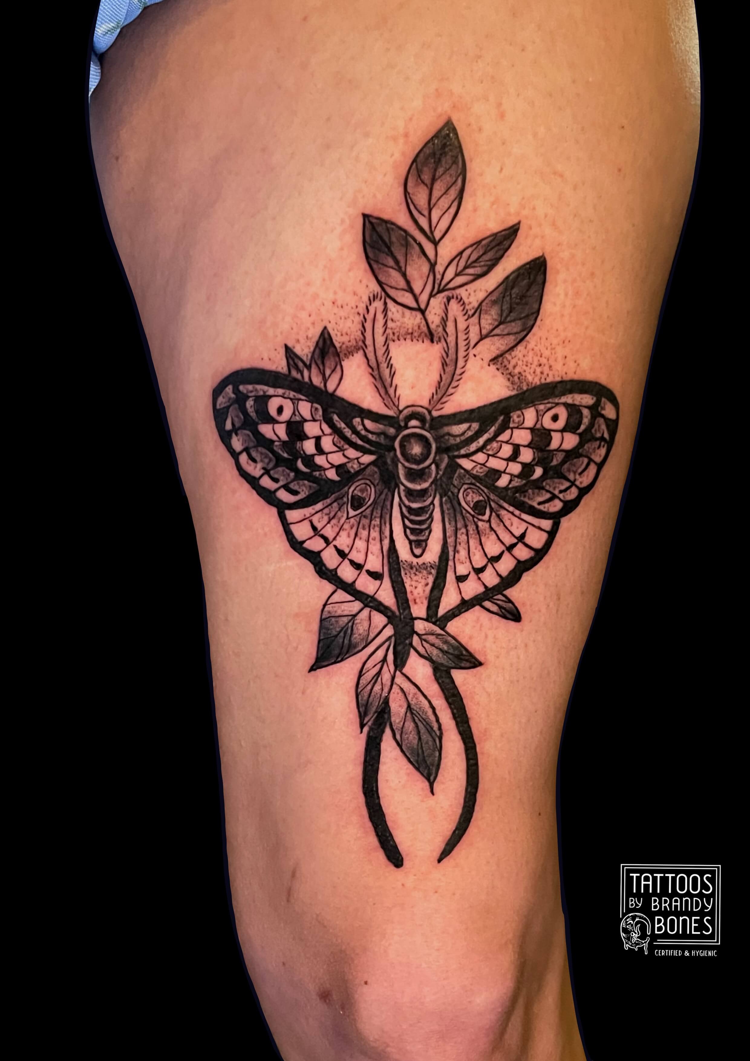 Black outline tattoo of a butterfly with detailed wings, connected to a branch with leaves.