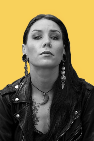 Black and white portrait of a woman with long dark hair wearing a leather jacket, large earrings, and a necklace with a crescent moon pendant, against a yellow background.