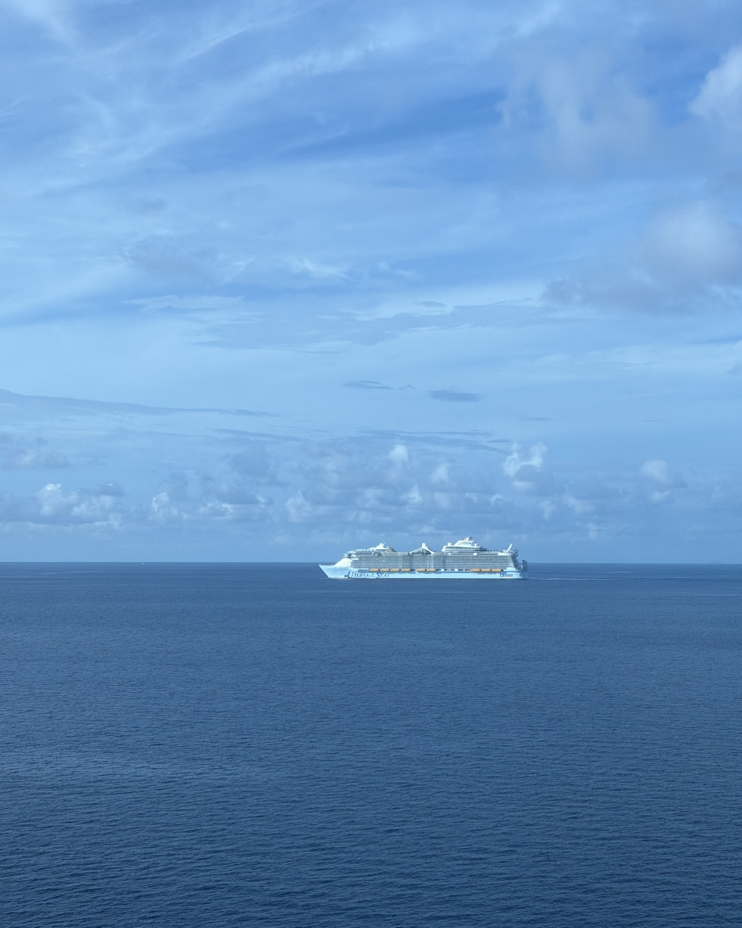 A large cruise ship sailing on calm open ocean under a partly cloudy sky.