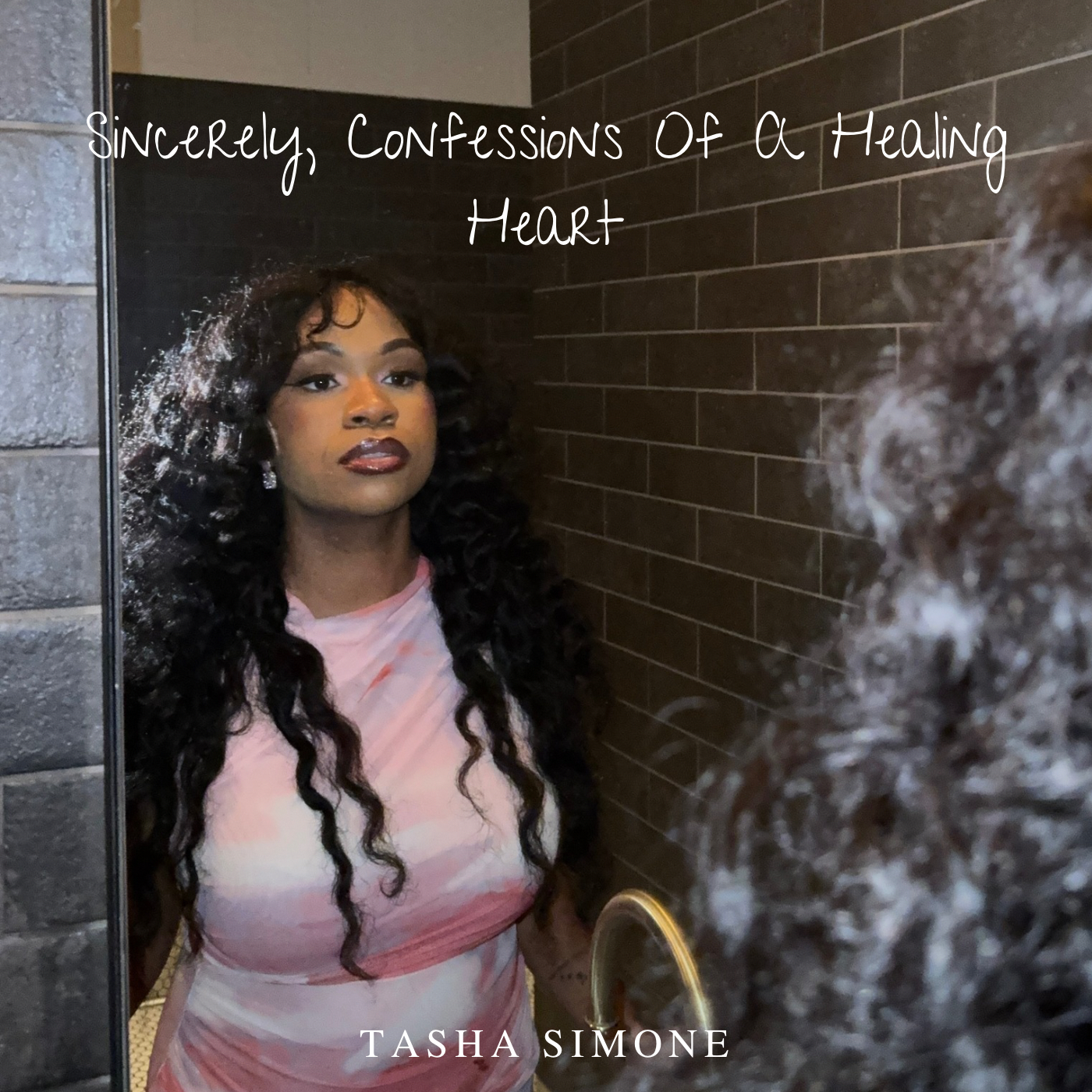 A woman with long, curly black hair and makeup stands in front of a mirror, looking at her reflection. She is wearing a pink and white dress, and the setting appears to be a bathroom or changing room with brick wall tiles. Text overlay on the image reads, "Sincerely, Confessions Of a Healing Heart," and at the bottom, the name "Tasha Simone" is displayed.