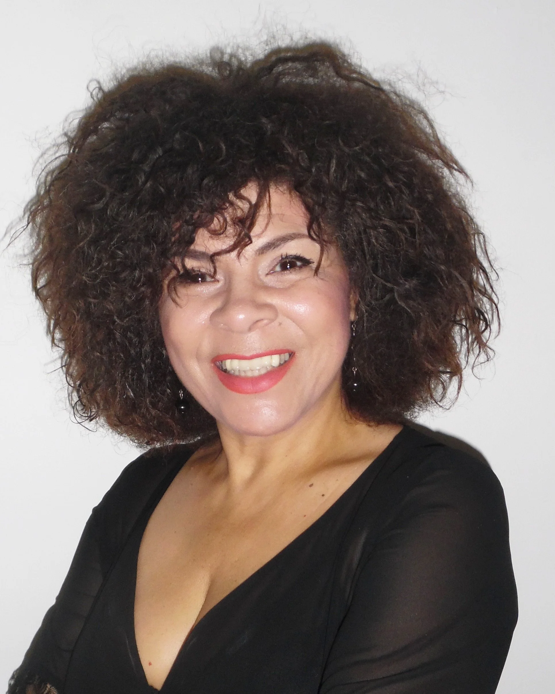 Woman smiling with brown curly hair, wearing a black top, against a white background.