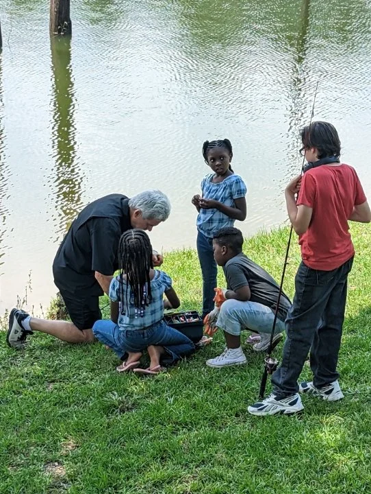 An elderly man and four children fishing and playing near a pond.