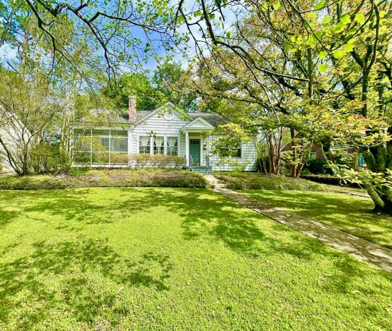 Front yard view of a white house with a green door, surrounded by green trees and a well-maintained lawn.