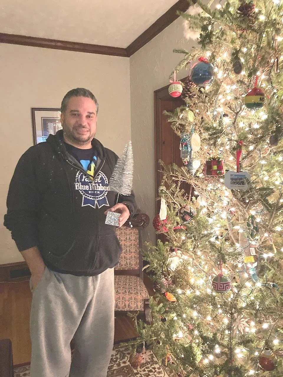 A man standing next to a decorated Christmas tree indoors at night.