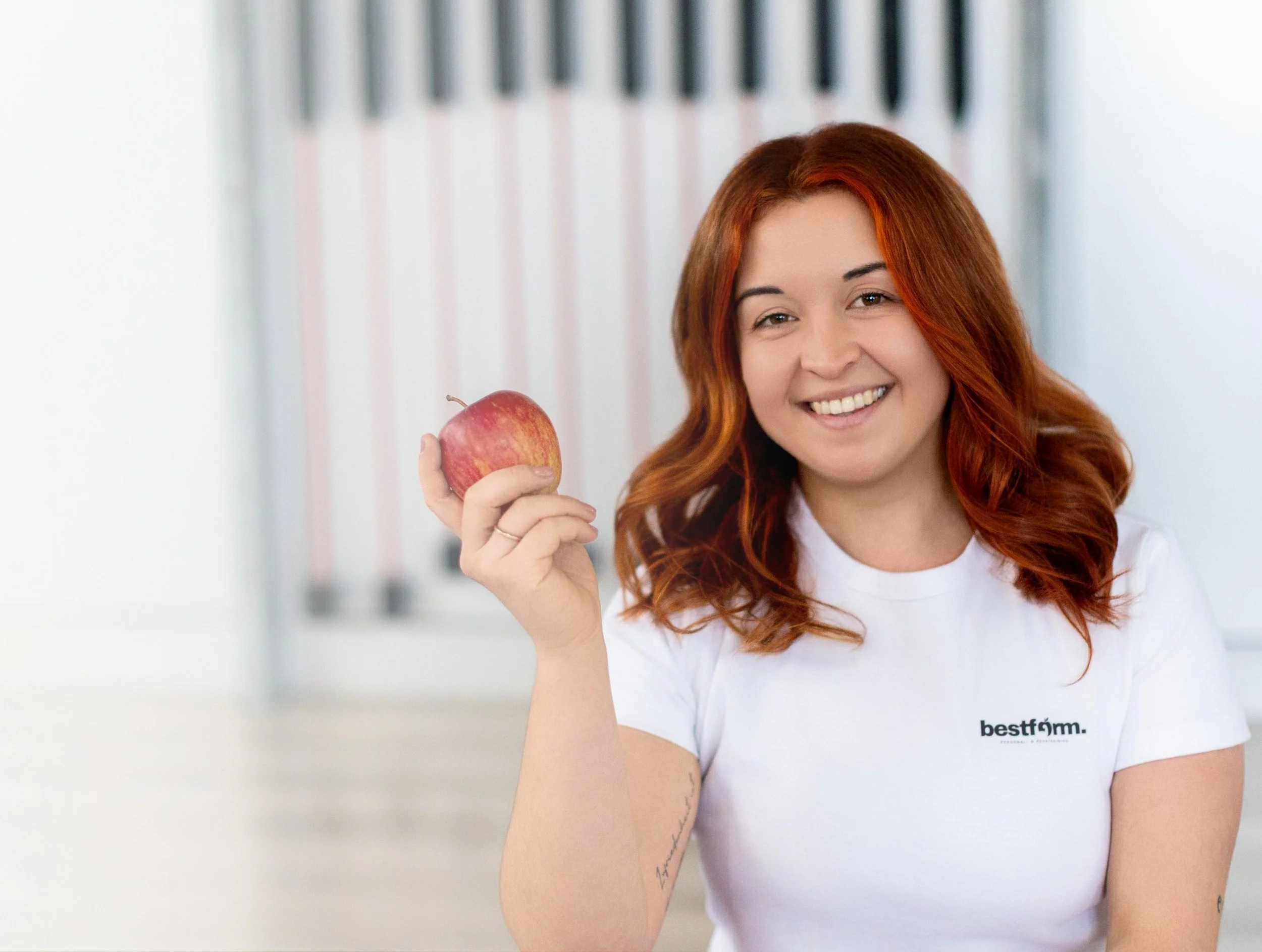 Eine Frauen mit roten Haaren hält einen Apfel in der Hand und lächelt.