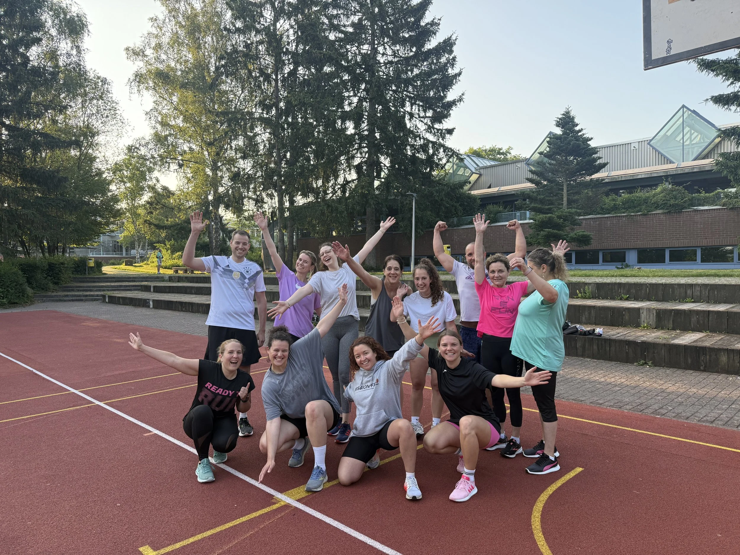 Gruppe von Menschen beim Sporttraining auf einer Laufbahn im Freien, lachend und fröhlich.