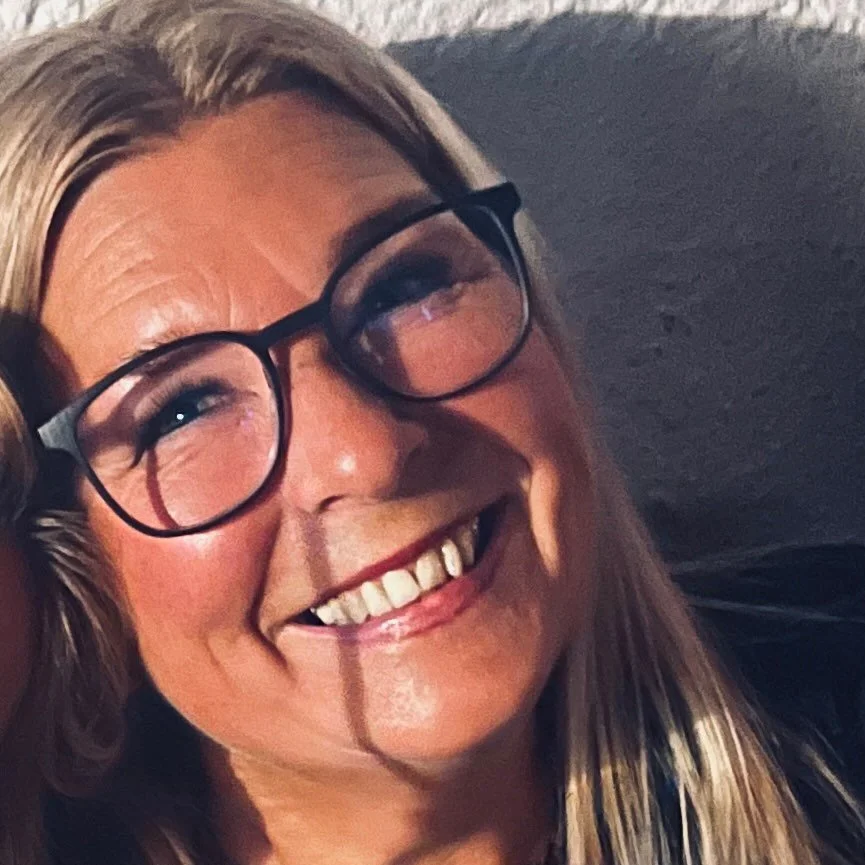 Ein lachender Mann mit Brille und blondem Haar vor hellem Hintergrund.