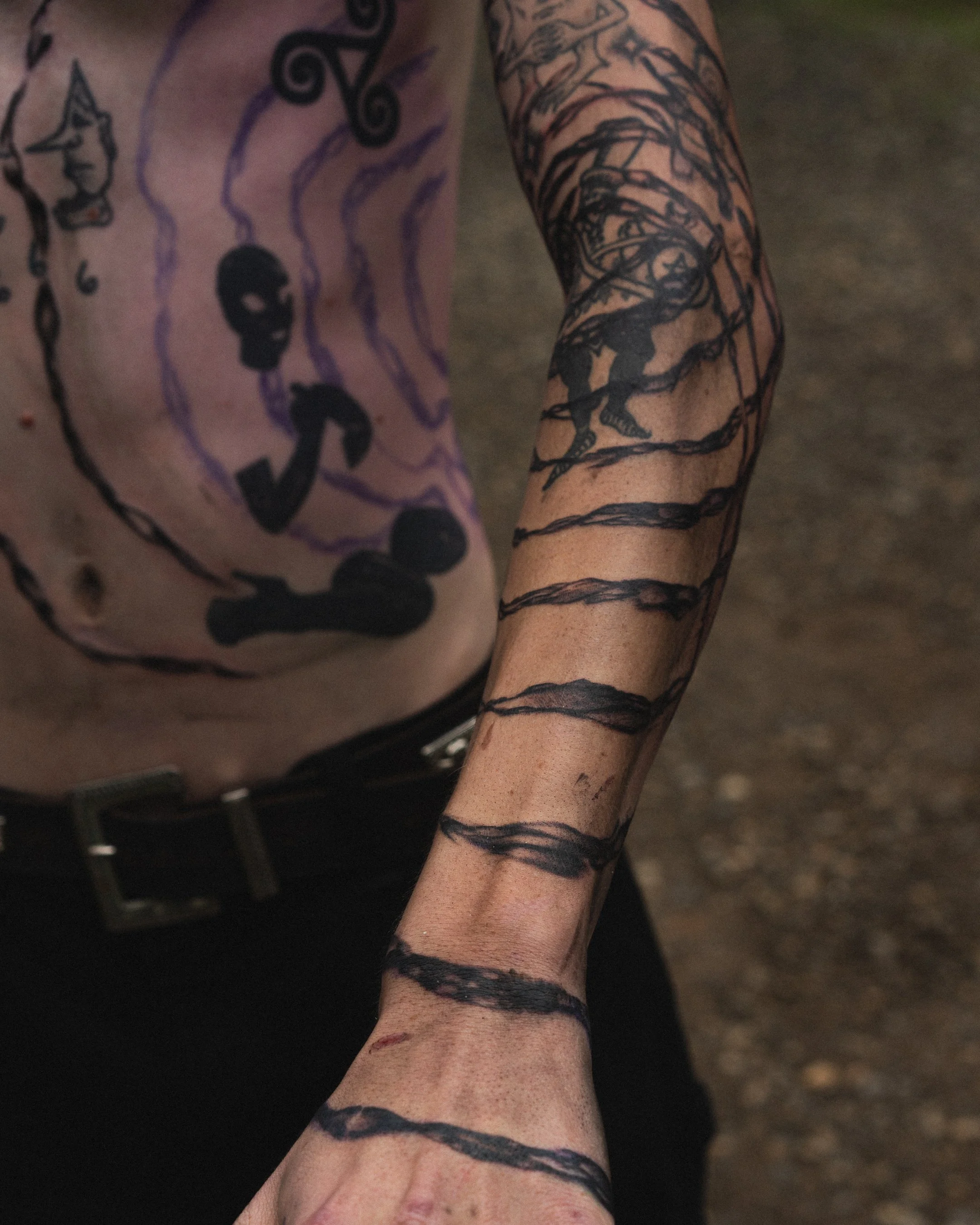Bras gauche d'une personne tatouée avec un dessin de cheval et des lignes en spirale noir, et bras droit avec un tatouage d'un homme enchaîné avec des lignes de contour sombre.