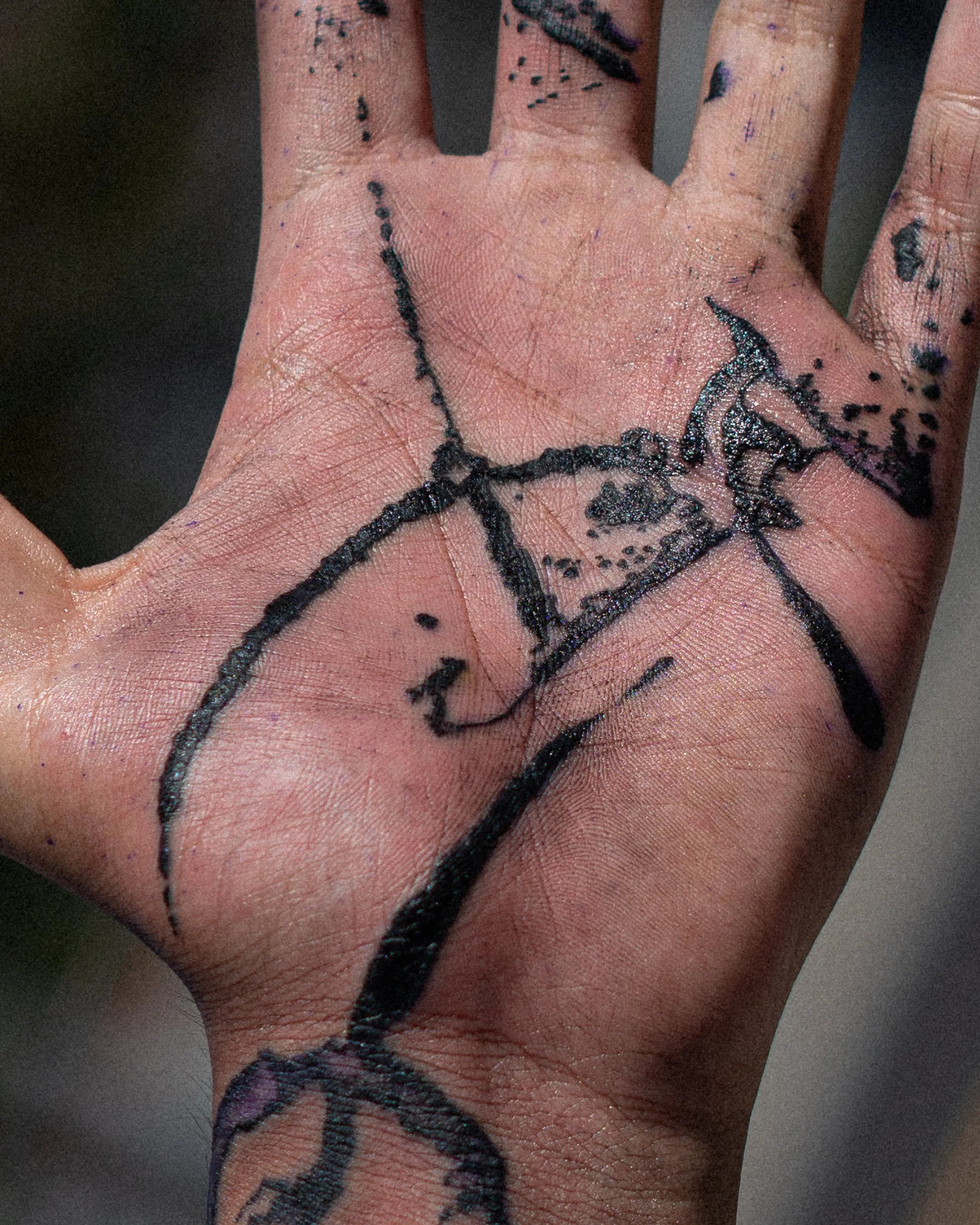 Main d'orteil avec tatouage de visage de squelette, quelques gouttes noires autour et des traces de peinture bleue